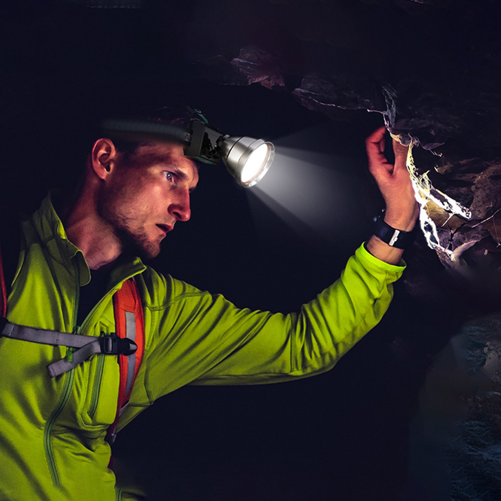 Ein Mann mit Stirnlampe erkundet eine dunkle Höhle und tastet die Felswand ab.