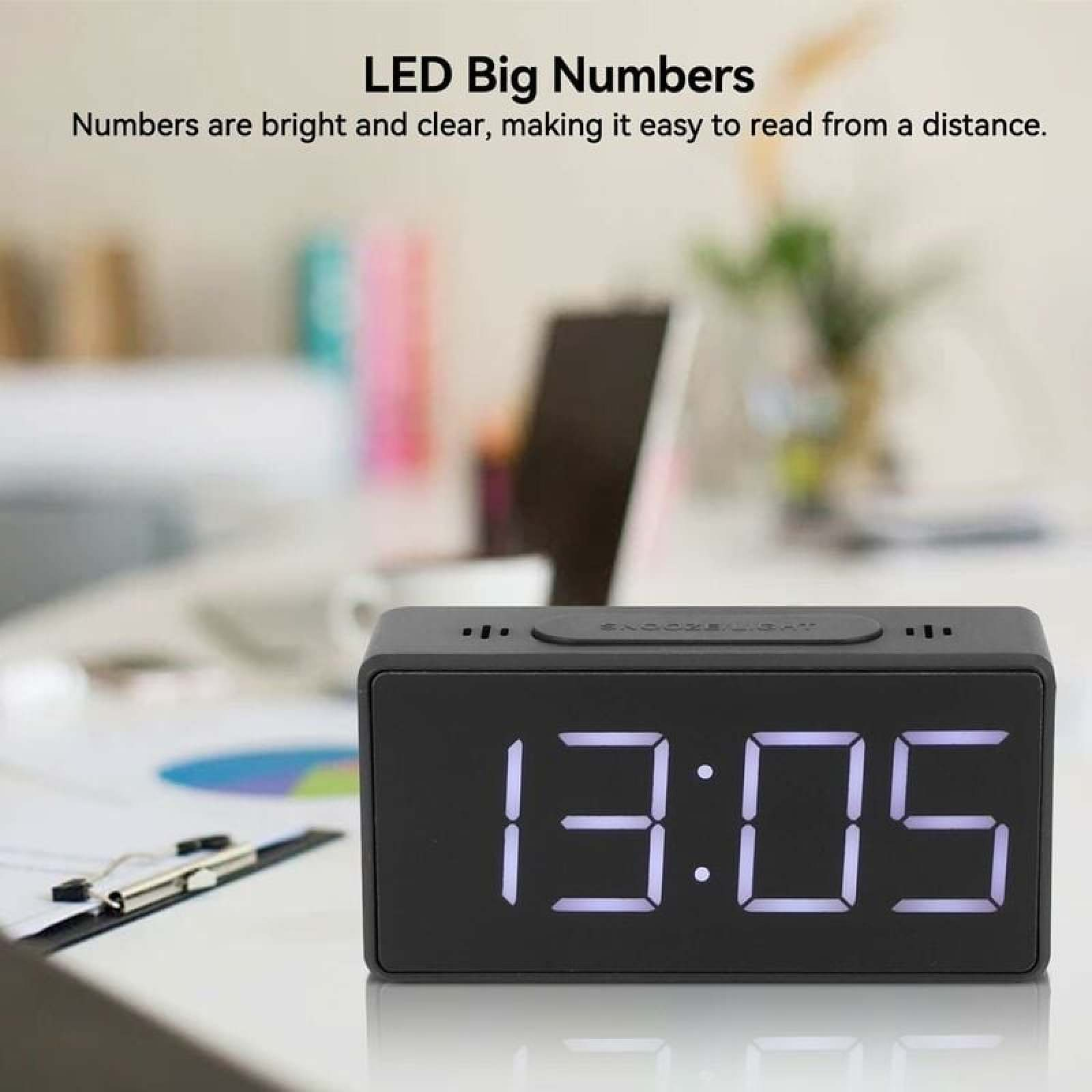 Ein schwarzer Digitalwecker zeigt 13:05 auf einem hellen Schreibtisch.