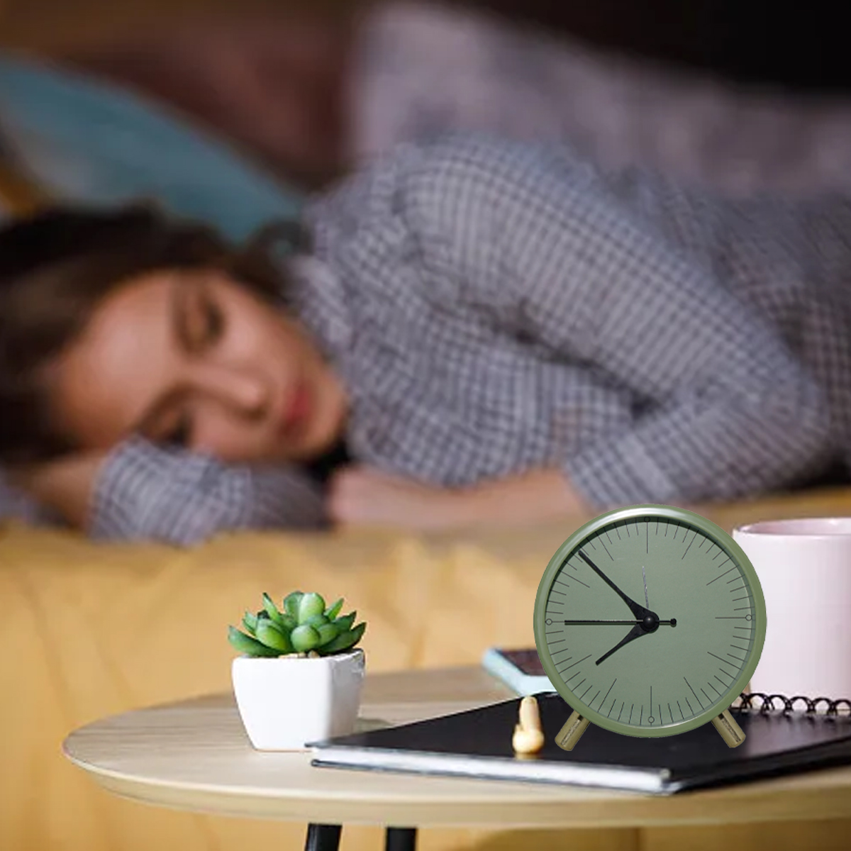 Eine Frau schläft auf einem Bett, ein Wecker steht auf einem Tisch daneben.