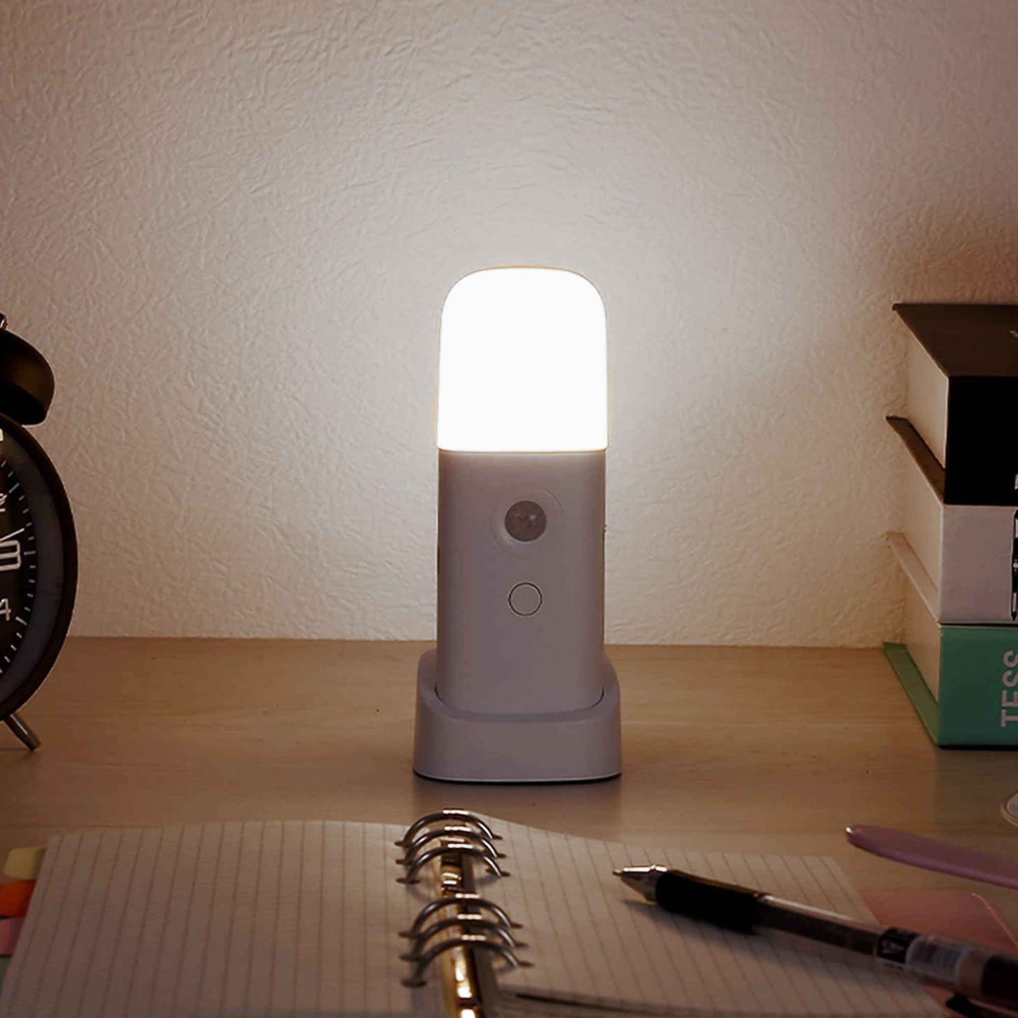 Ein kleiner Nachttisch mit Lampe, Notizbuch und Stift auf einem Schreibtisch.