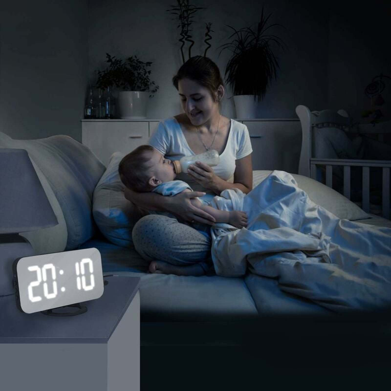 Mutter füttert Baby mit Fläschchen im Bett bei Nacht, Digitaluhr zeigt 20:10.
