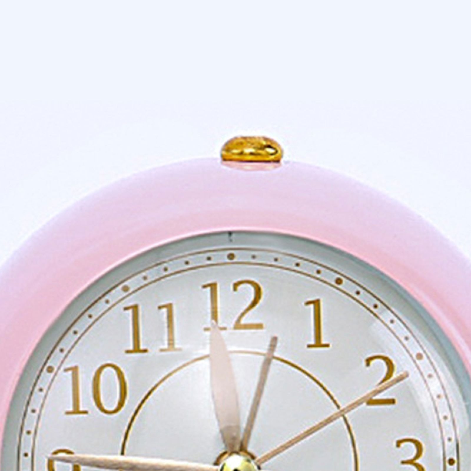 Ein rosa Wecker mit goldenem Knopf und Zifferblatt. Die Zeiger sind bei 12:45.