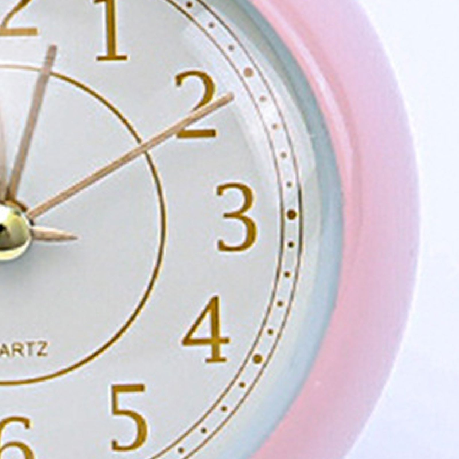 Nahaufnahme eines rosa Weckers mit goldenen Zeigern und Ziffern auf einem weißen Zifferblatt.