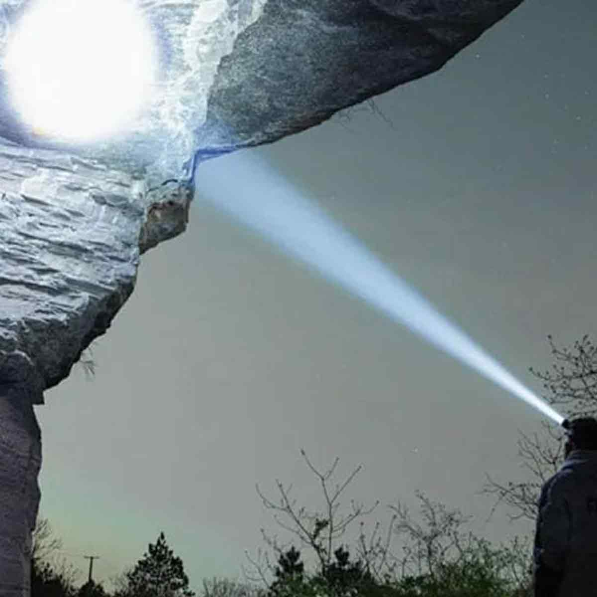 Ein Mann mit Stirnlampe leuchtet auf Felsen unter einem Nachthimmel.
