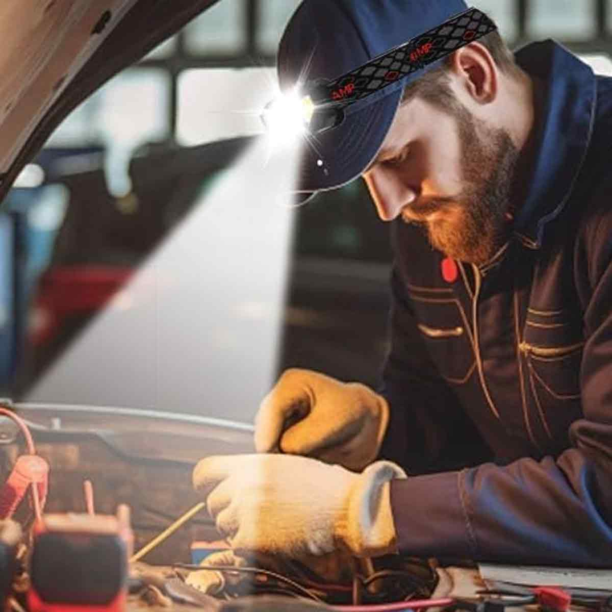 Mechaniker mit Stirnlampe repariert Motor. Hände in Handschuhen arbeiten an Kabeln.