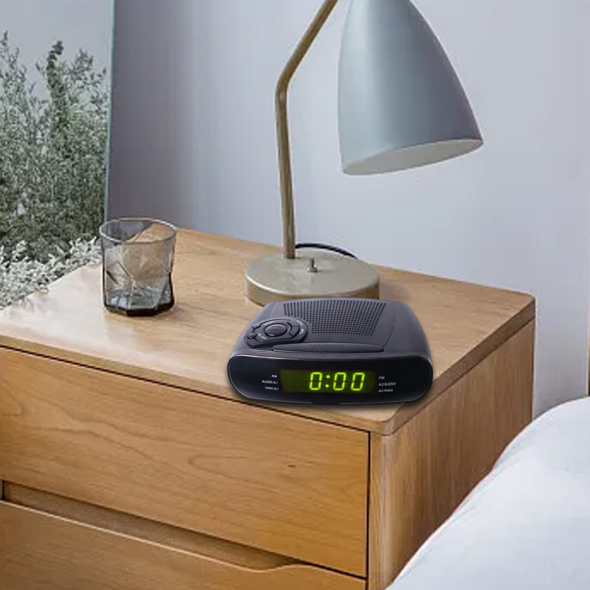 Ein schwarzer Digitalwecker mit grünem Display steht auf einem Holztisch neben einer Lampe.
