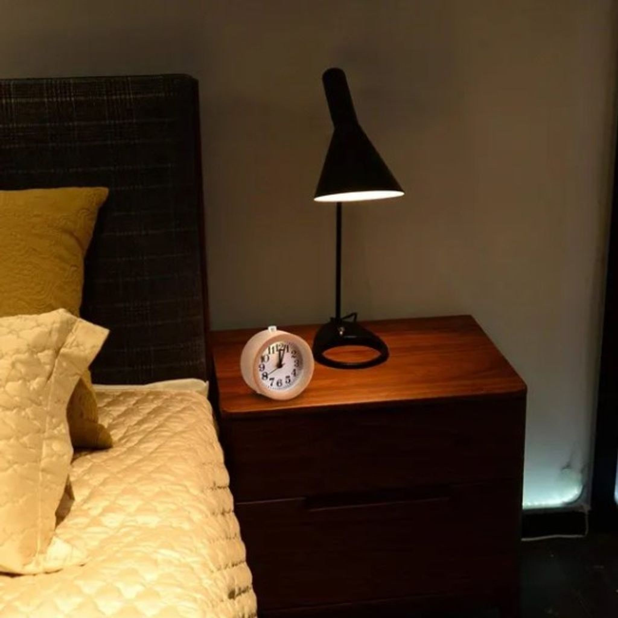 Ein Nachttisch mit Lampe und Wecker neben einem Bett.