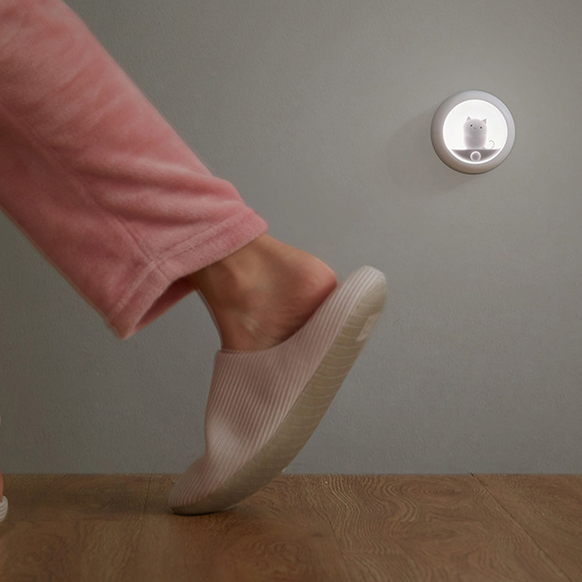 Eine Person in rosa Hausschuhen betritt einen Holzboden. Ein Nachtlicht mit Katzendesign ist an der Wand.