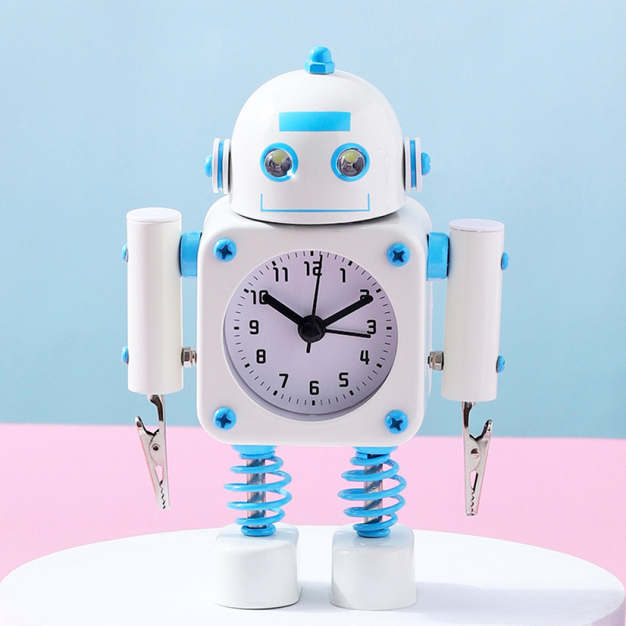 Ein weißer Roboter-Wecker mit blauen Akzenten steht vor einem hellblauen und rosa Hintergrund.