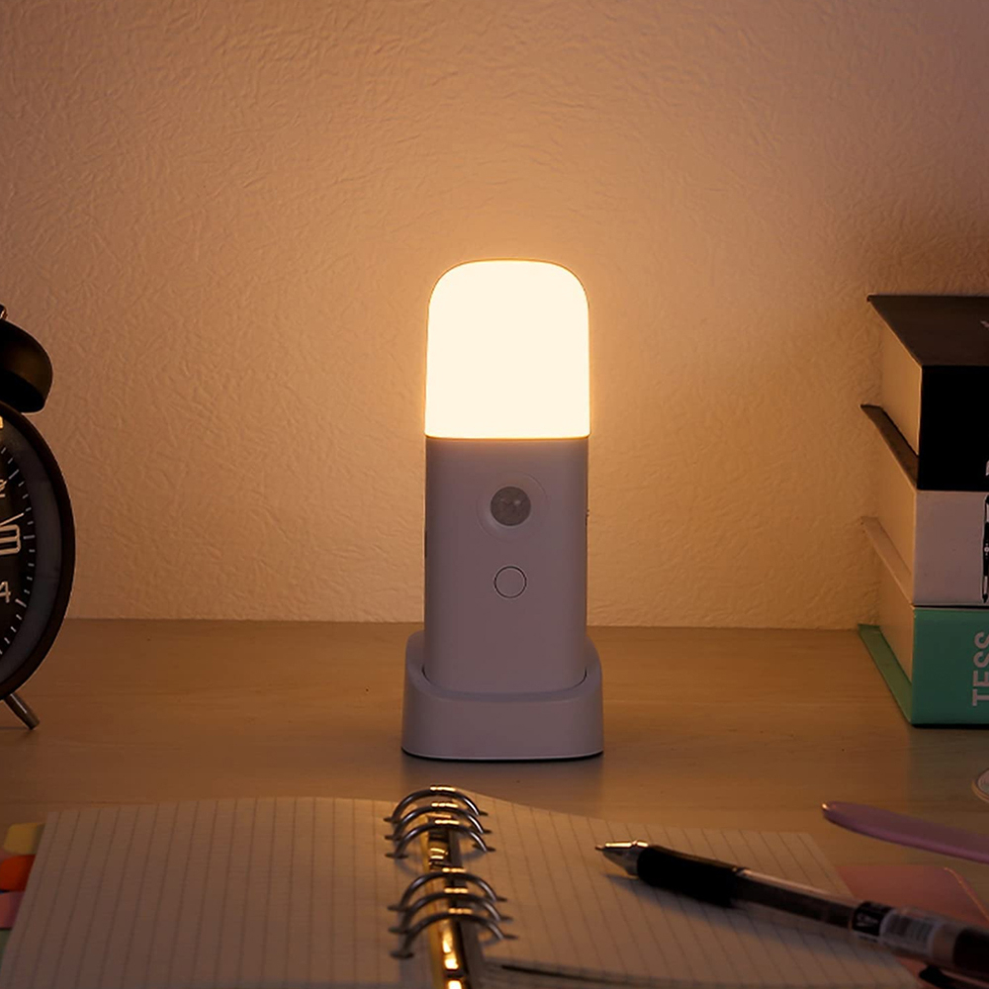 Ein Nachttisch mit Lampe, Notizbuch, Stift und Uhr.