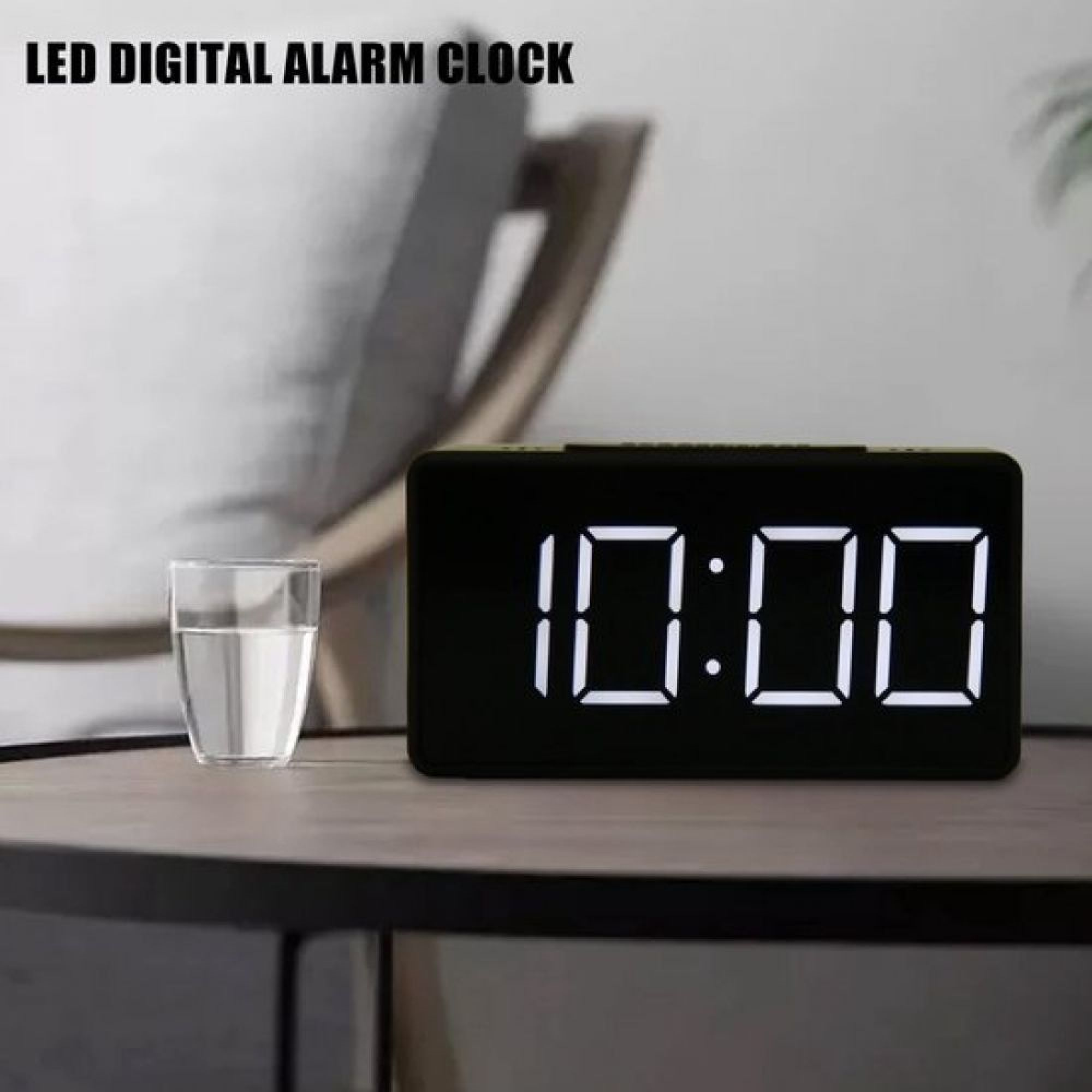 Schwarze Digitaluhr zeigt 10:00 auf einem Holztisch neben einem Glas Wasser.