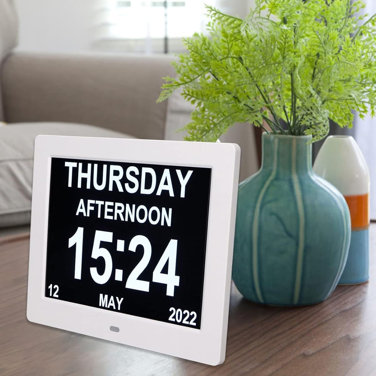 Digitaluhr zeigt Donnerstag, 15:24 Uhr, 12. Mai 2022, mit Pflanzen im Hintergrund.