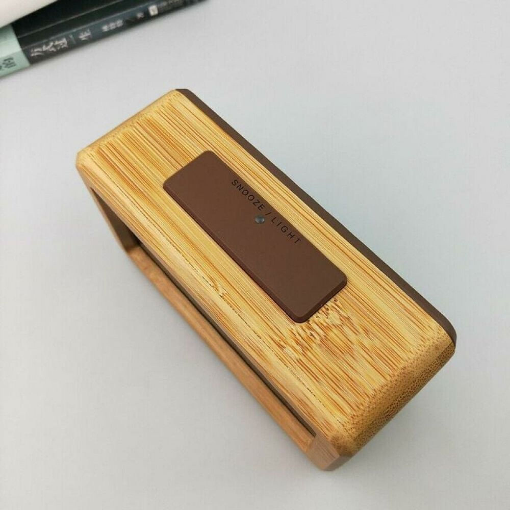 Ein hölzerner Wecker mit brauner Snooze/Licht-Taste und einem kleinen Lämpchen.