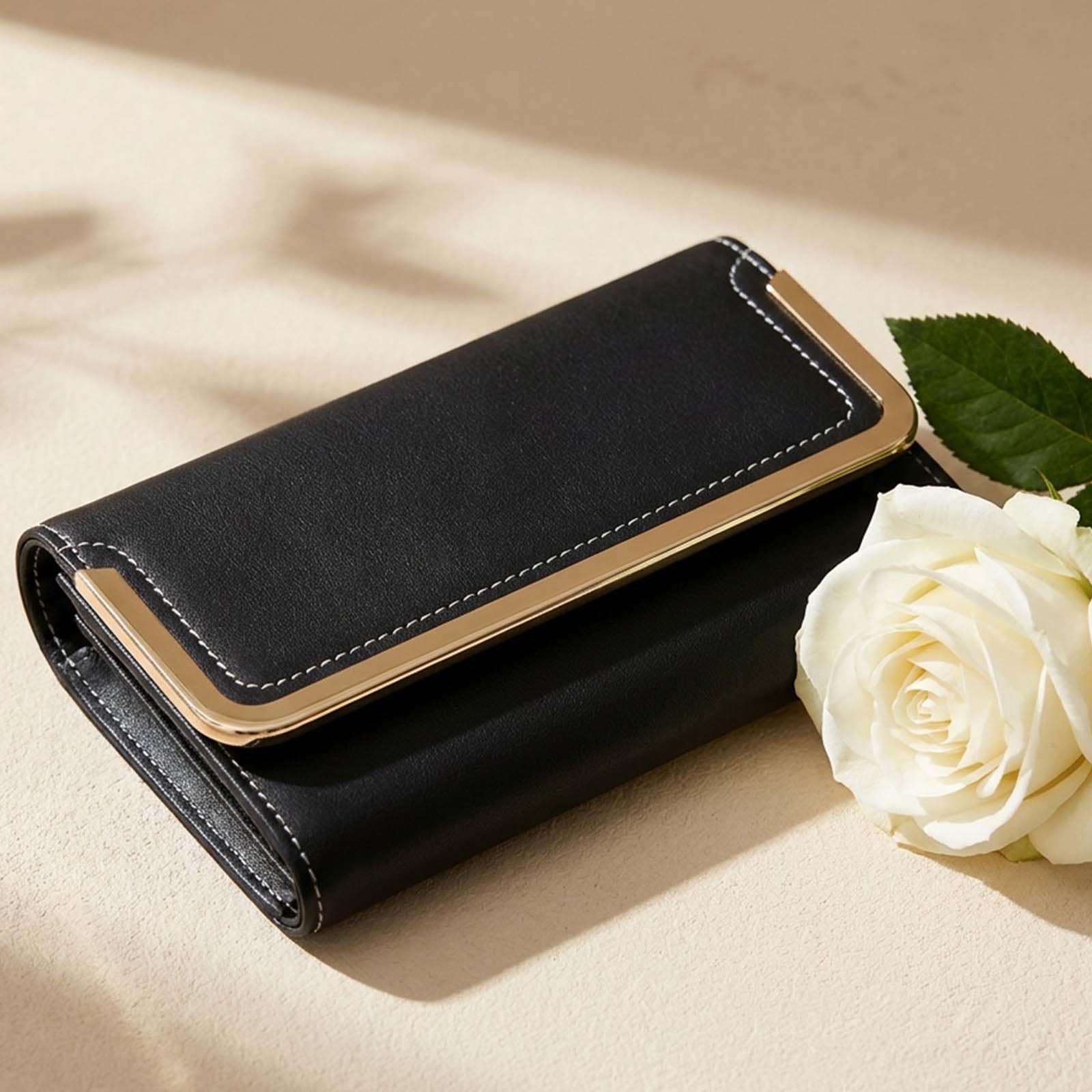 Schwarze Brieftasche mit goldener Zierleiste und weißer Rose daneben.