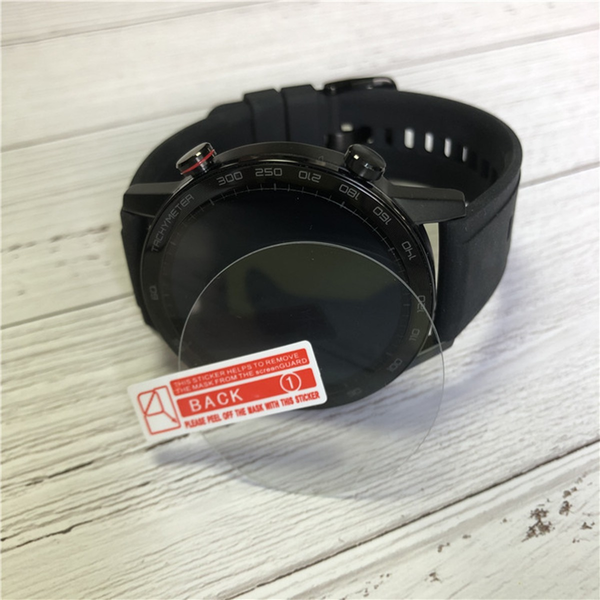 Smartwatch nero con protezione schermo e adesivo rosso su sfondo di legno.