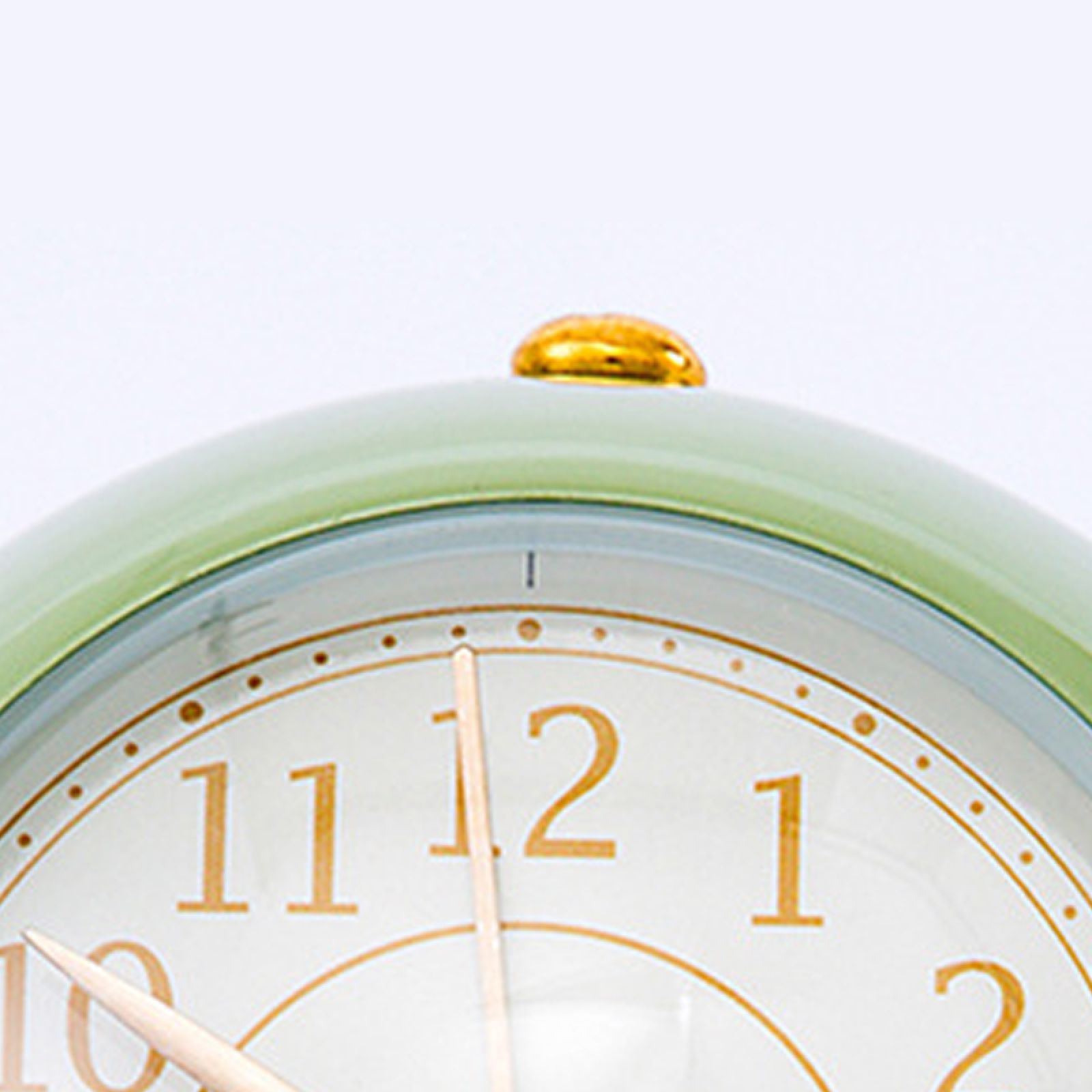 Grüne Uhr mit goldenem Knopf oben und goldenen Ziffern auf weißem Zifferblatt.