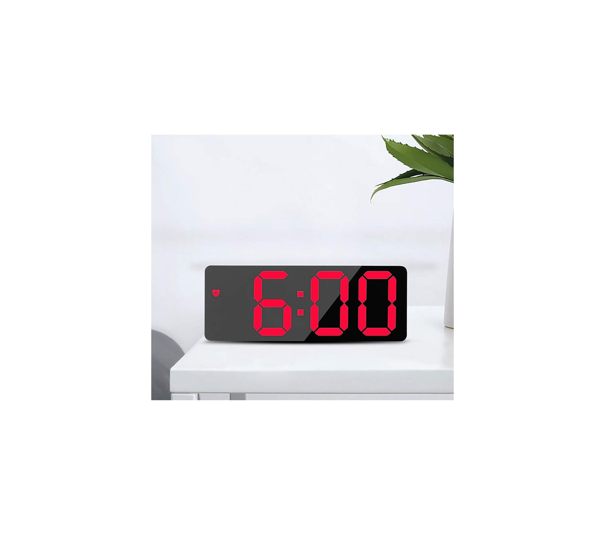 Ein digitaler Wecker zeigt 6:00 auf schwarzem Display. Ein grünes Blatt ist im Hintergrund.