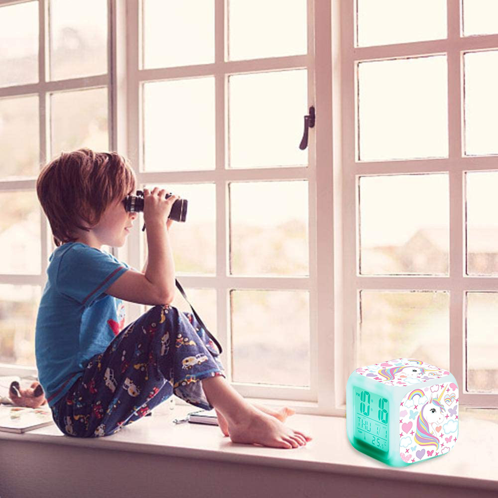 Ein Junge mit Fernglas sitzt am Fenster neben einem Wecker mit Einhorn-Motiv.