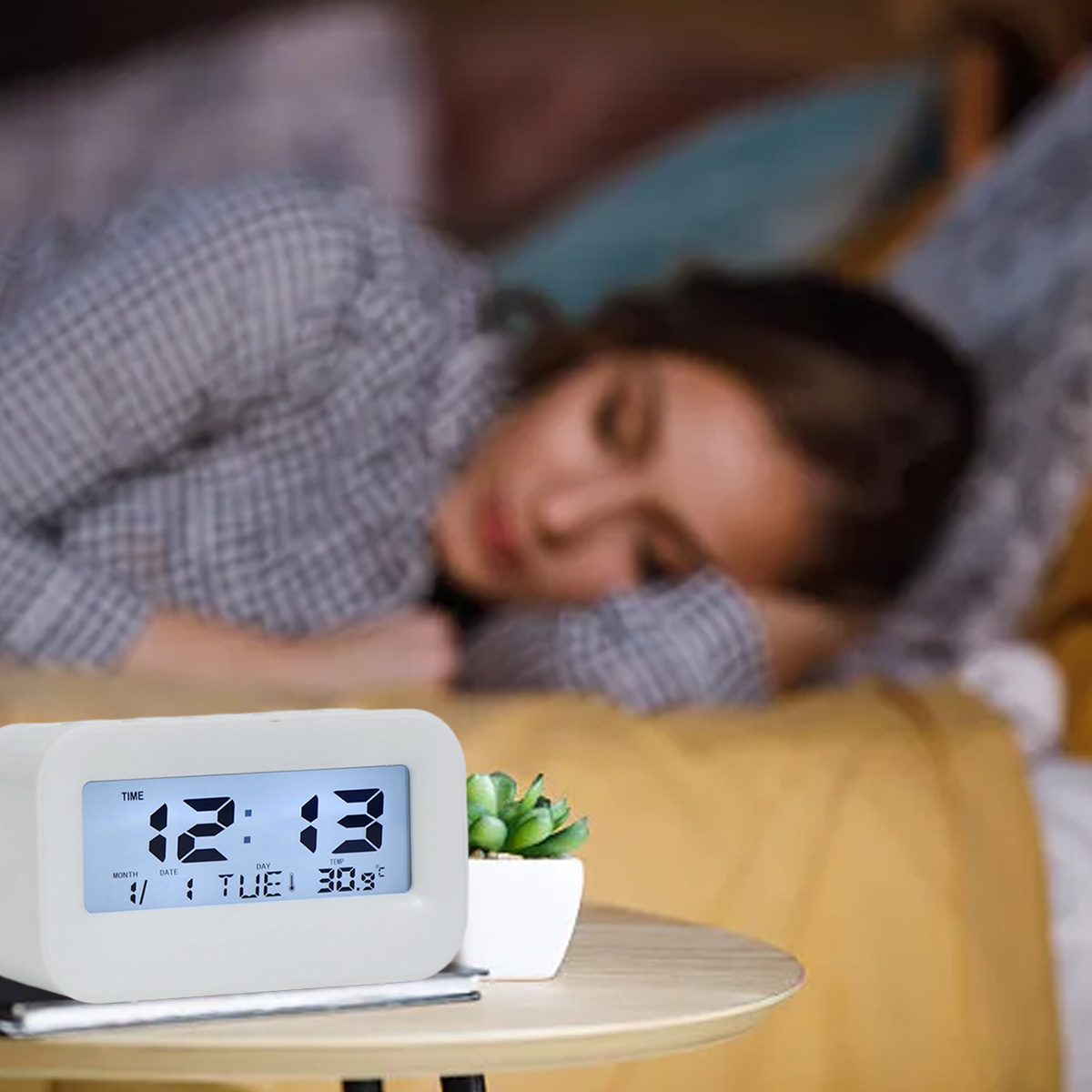 Eine Frau schläft auf einem Bett, ein digitaler Wecker steht daneben.