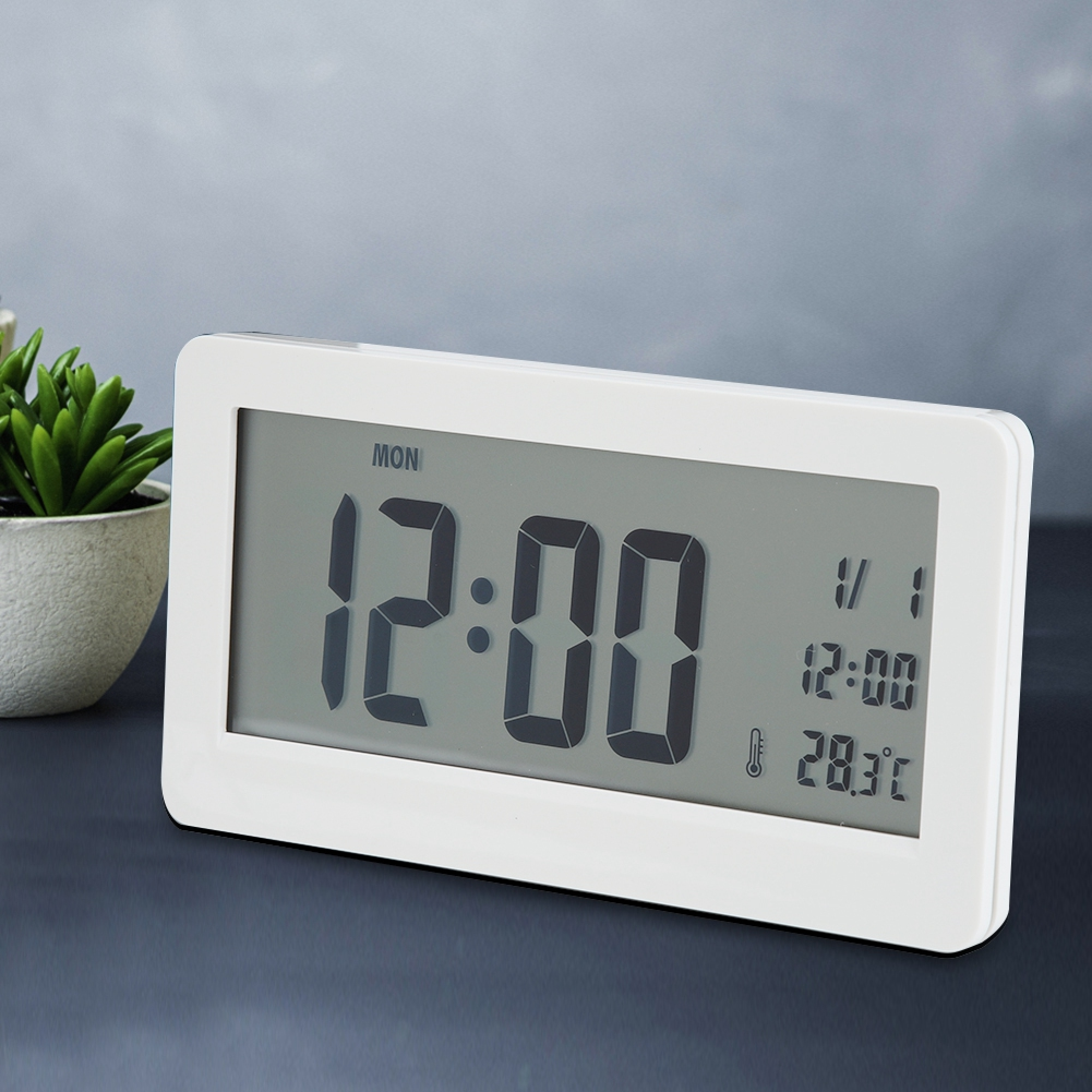 Ein weißer Digitalwecker zeigt Montag, 12:00 Uhr und 28,3 Grad Celsius an.