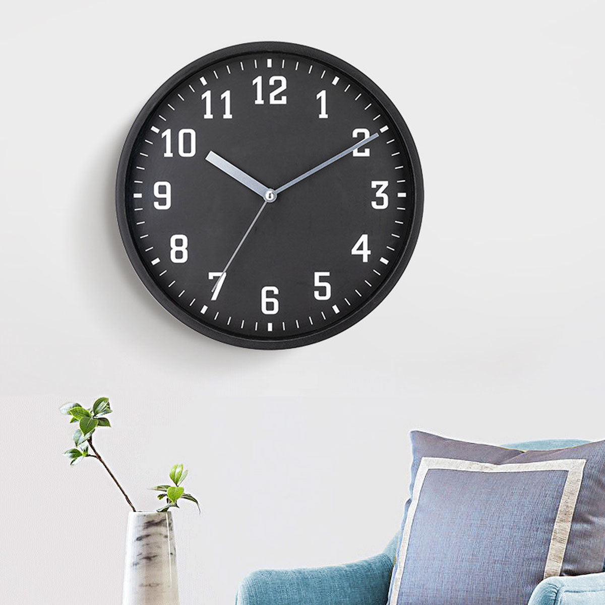 Eine schwarze Wanduhr mit weißen Zahlen hängt an einer weißen Wand.