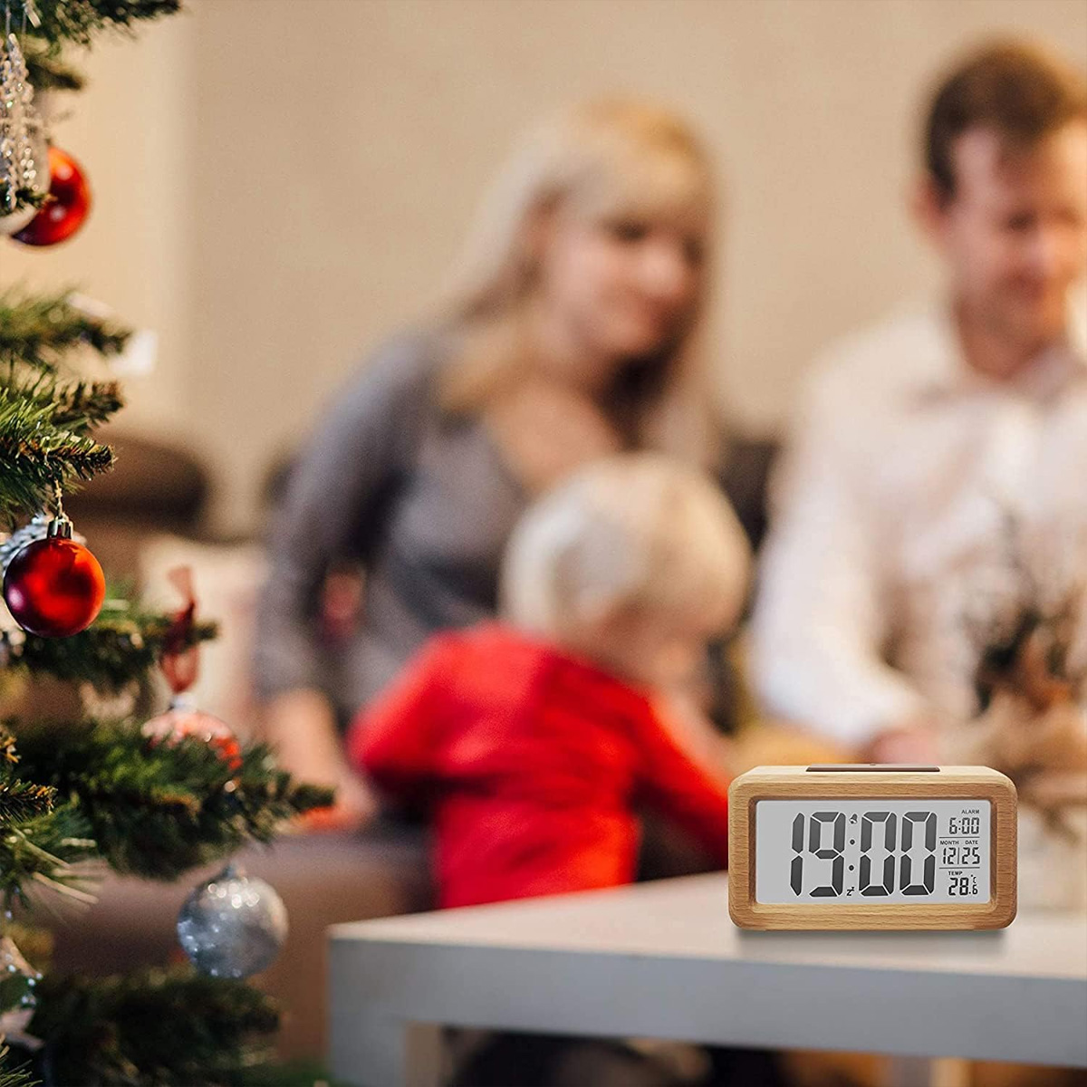Ein hölzerner Digitalwecker zeigt 19:00 Uhr an, im Hintergrund eine Familie.