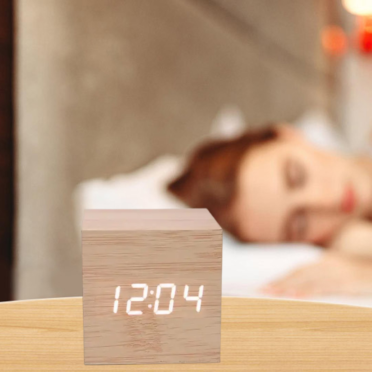 Ein Holzwecker zeigt 12:04 an, eine Person schläft im Hintergrund.
