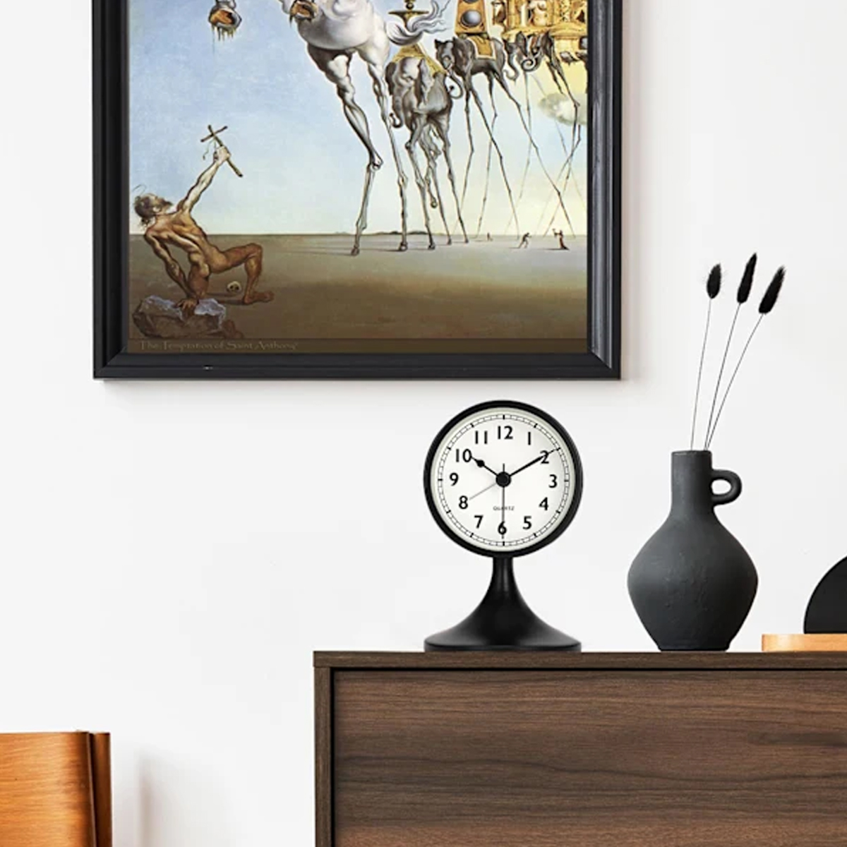 Ein surrealistisches Gemälde über einem schwarzen Nachttisch mit Uhr und Vase.