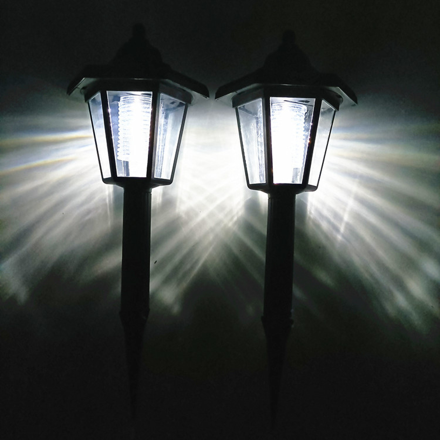 Zwei leuchtende Solar-Gartenleuchten im Dunkeln mit Lichtstrahlen.