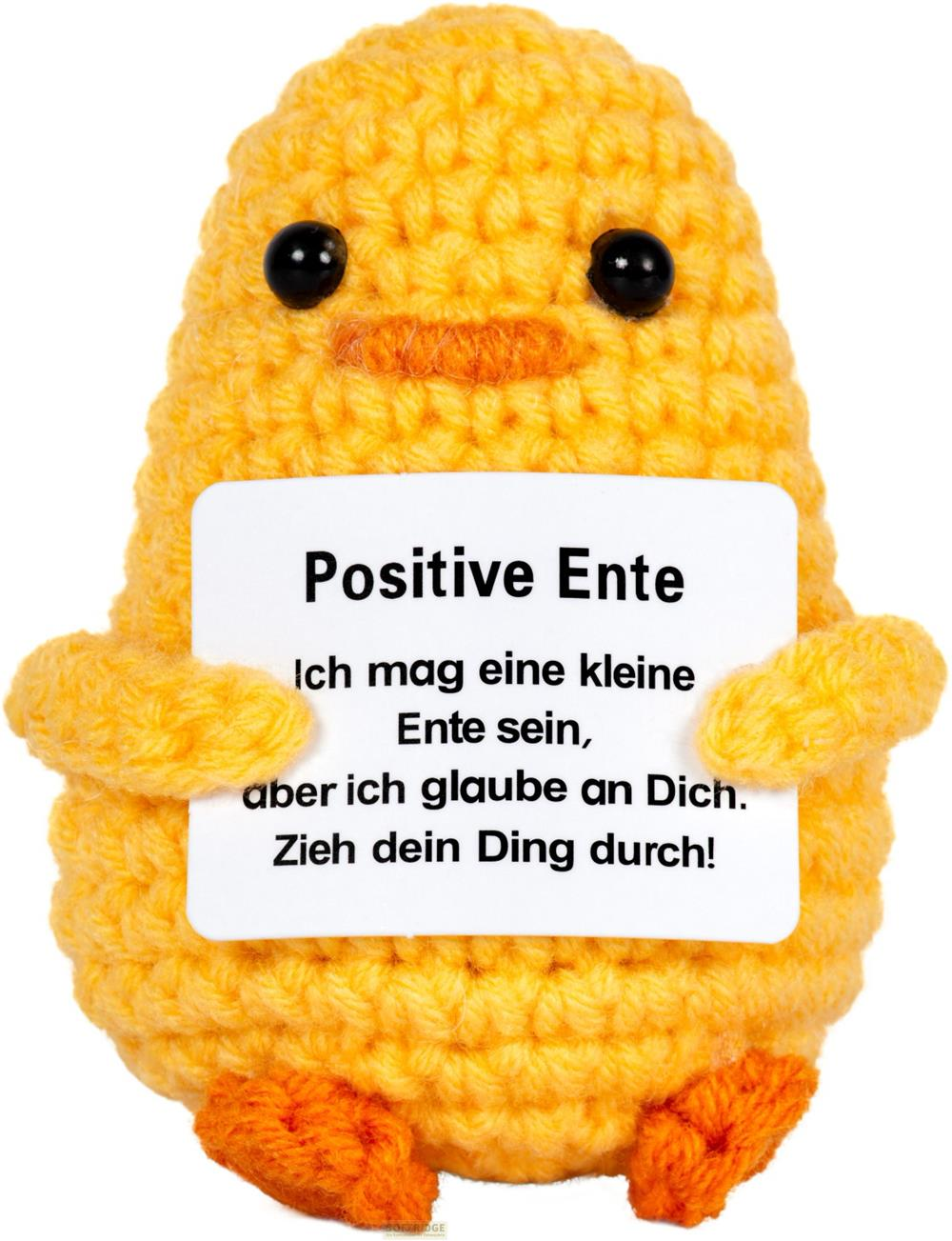 Un canard jaune crocheté tient une pancarte avec du texte allemand.