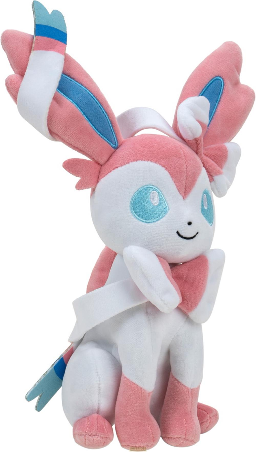 Une peluche rose et blanche avec des yeux bleus et des rubans roses.