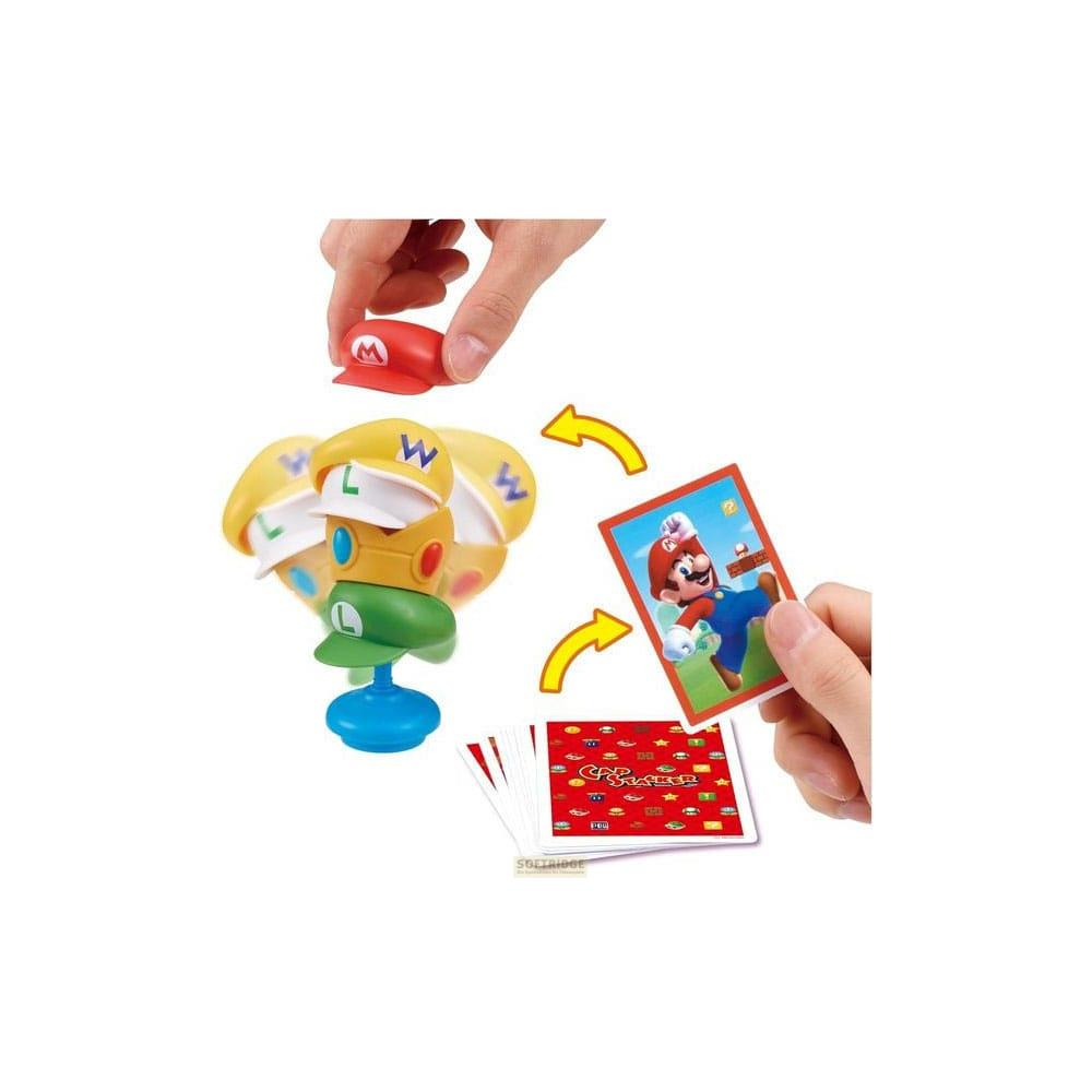 Un juguete de Mario con sombreros y cartas. Un pulgar sostiene un sombrero rojo con una M.