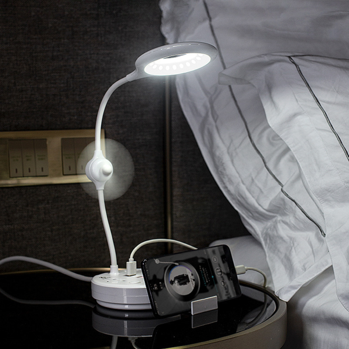 Eine weiße Schreibtischlampe mit LED und kleinem Ventilator leuchtet neben einem Bett.