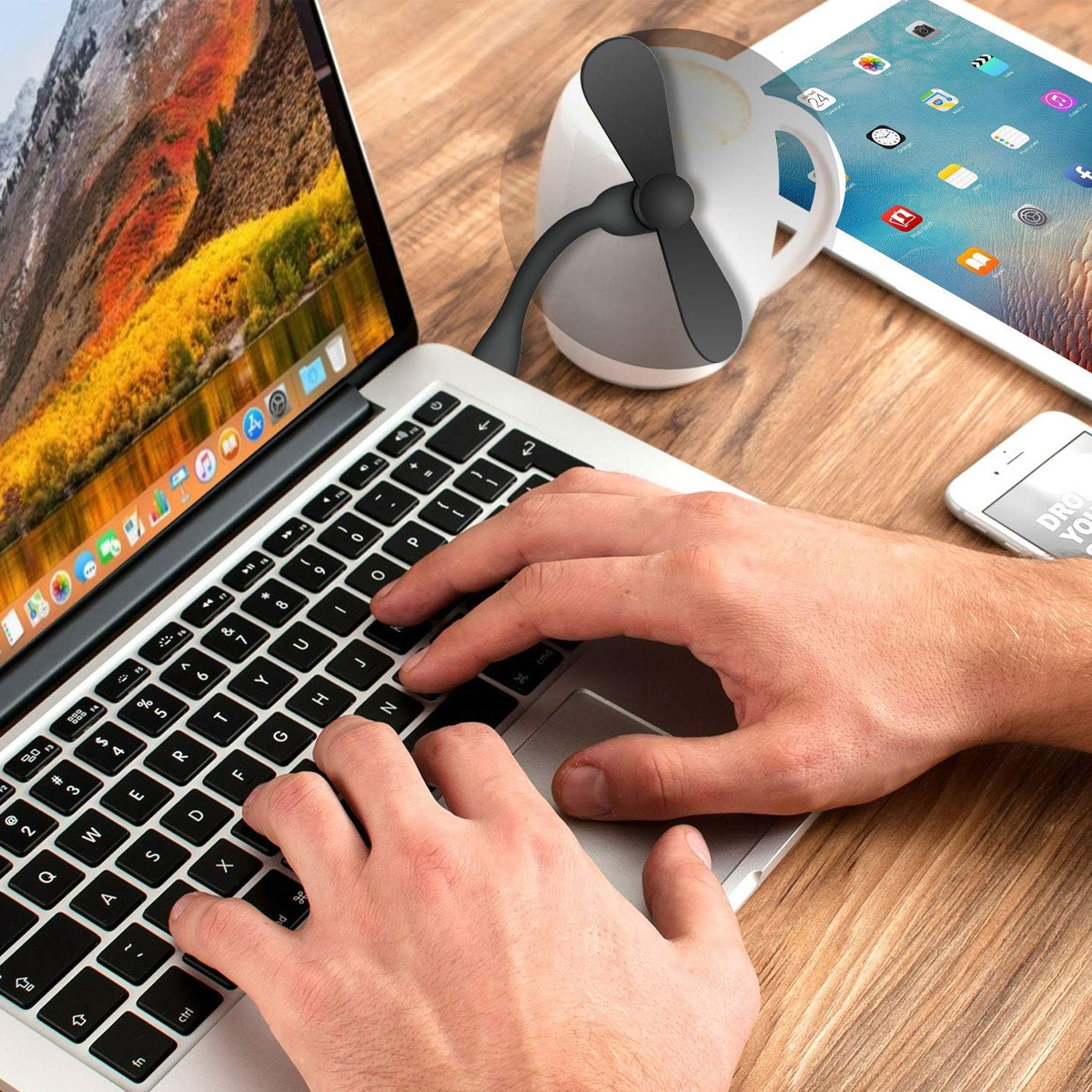 Hände tippen auf einem Laptop, daneben ein Mini-USB-Ventilator, Tablet und Smartphone.