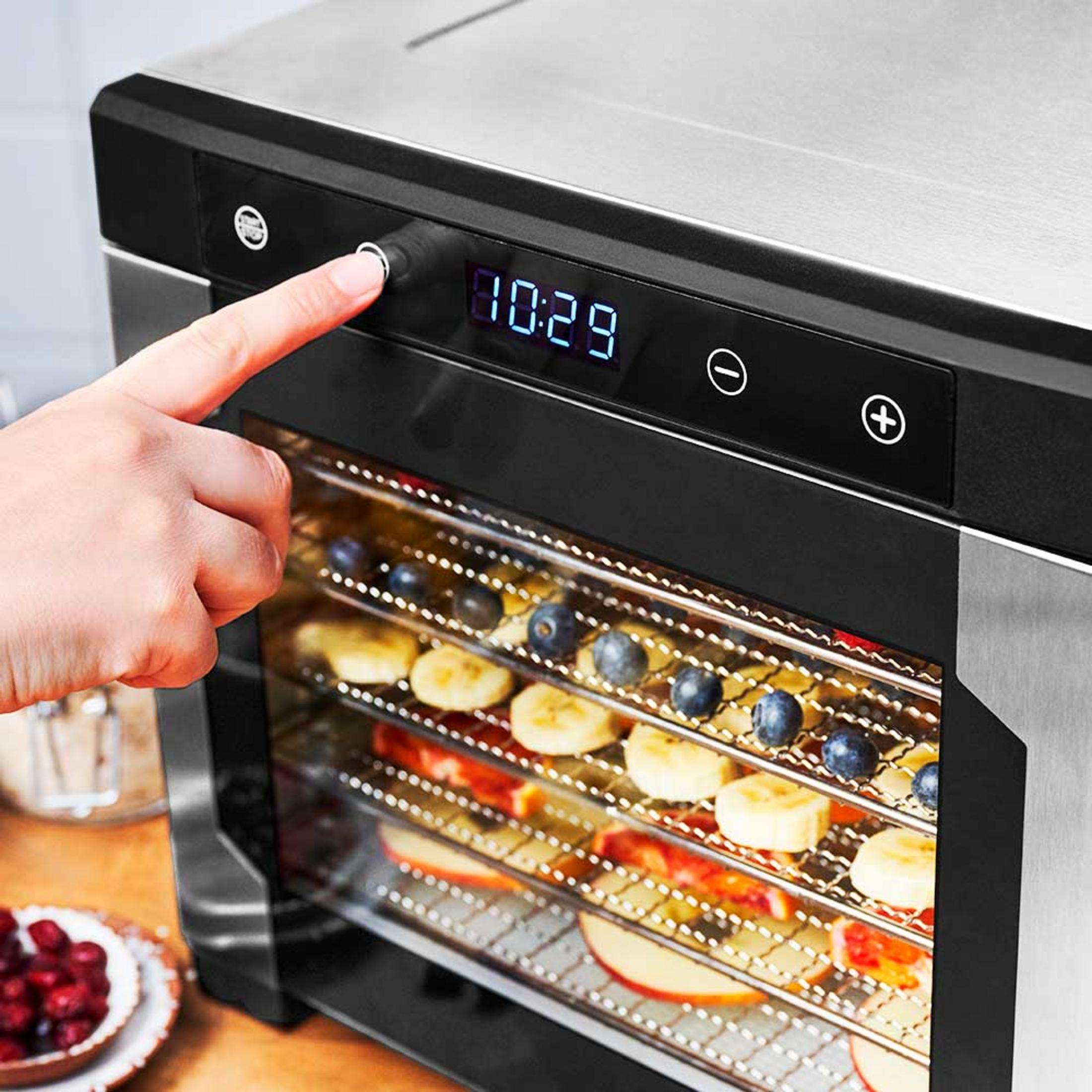 Un dito preme il pulsante di avvio di un essiccatore con strati di frutta.