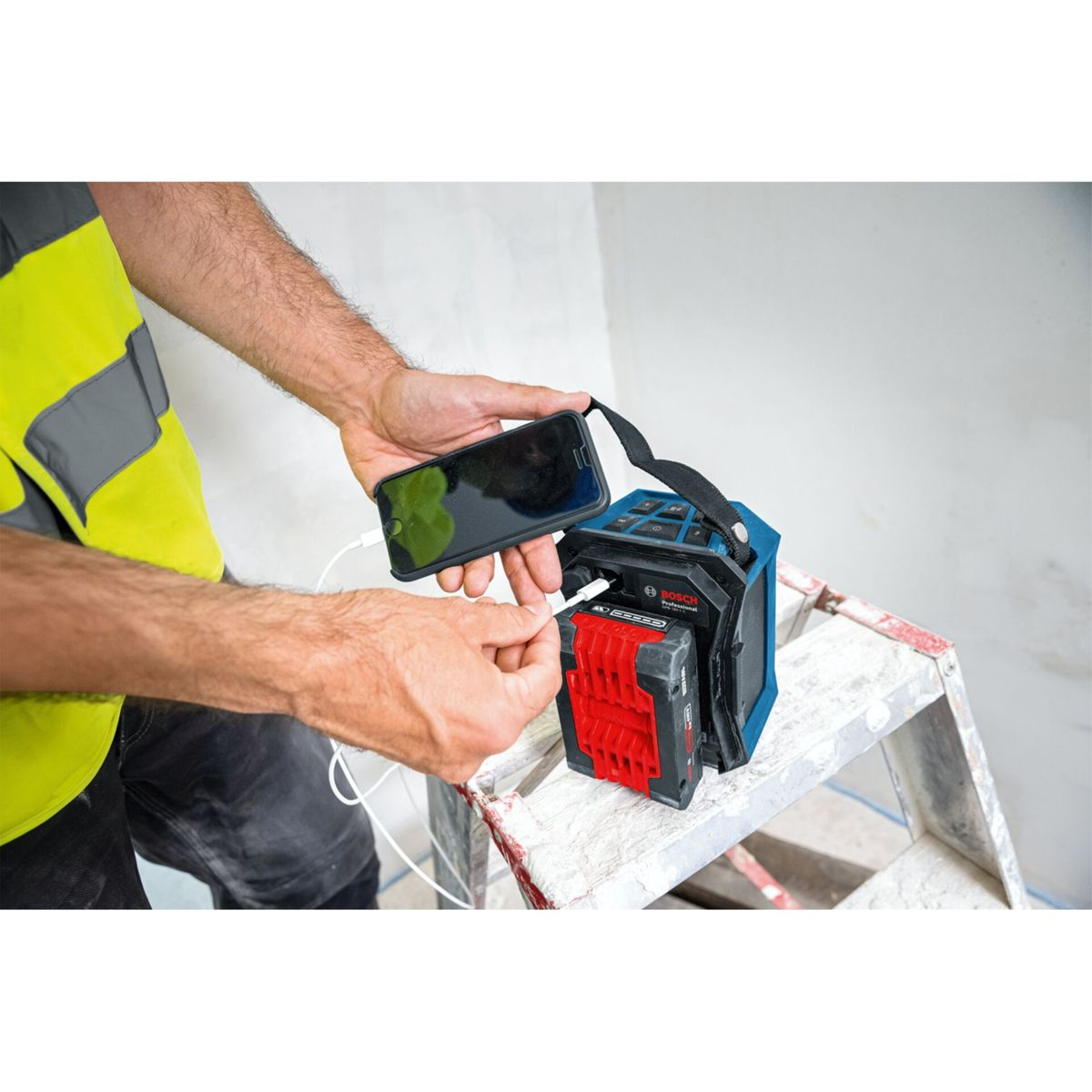 Uomo carica smartphone con batteria Bosch su una scala.