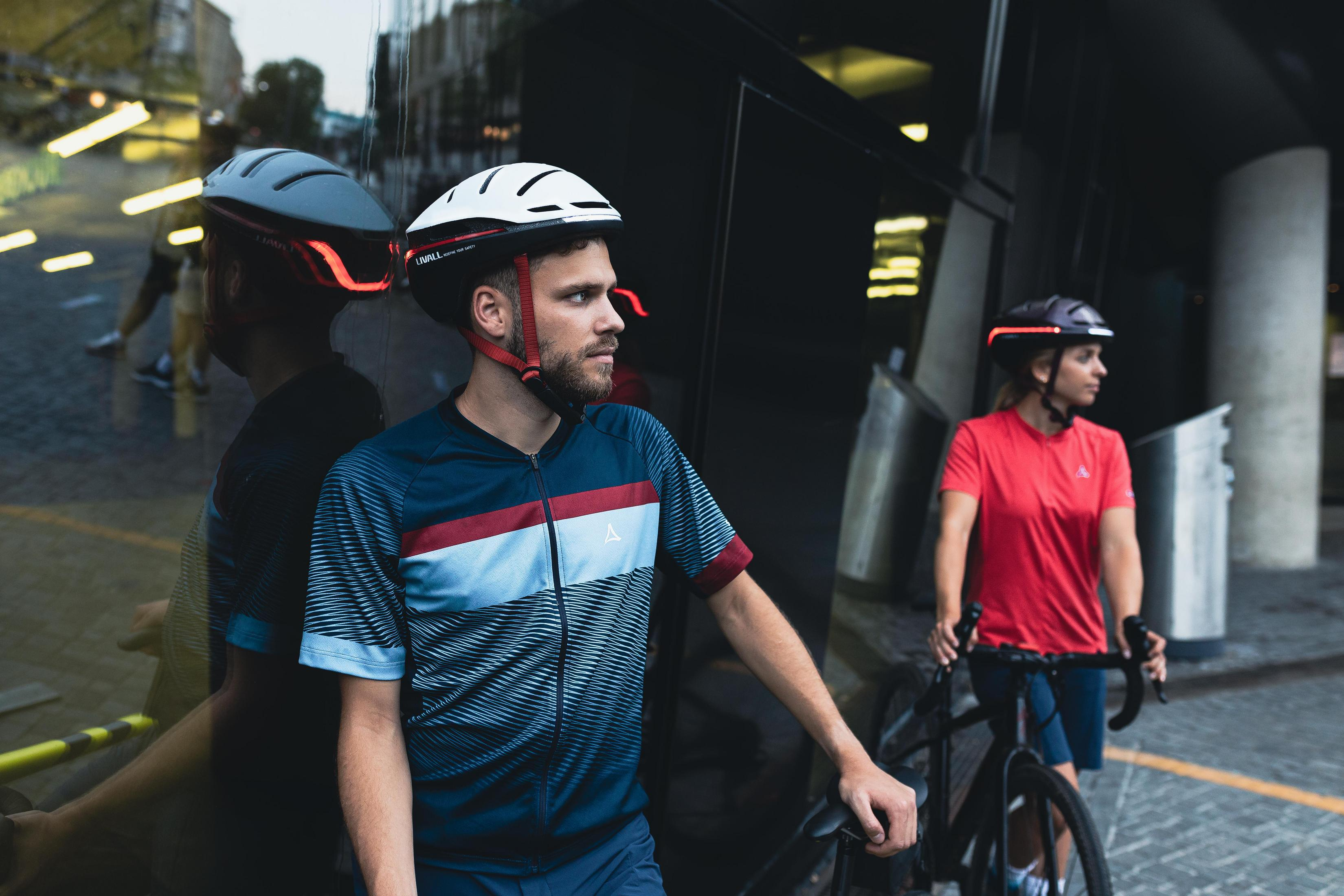 Due ciclisti con casco stanno fianco a fianco, uno in blu, l'altro in rosso.