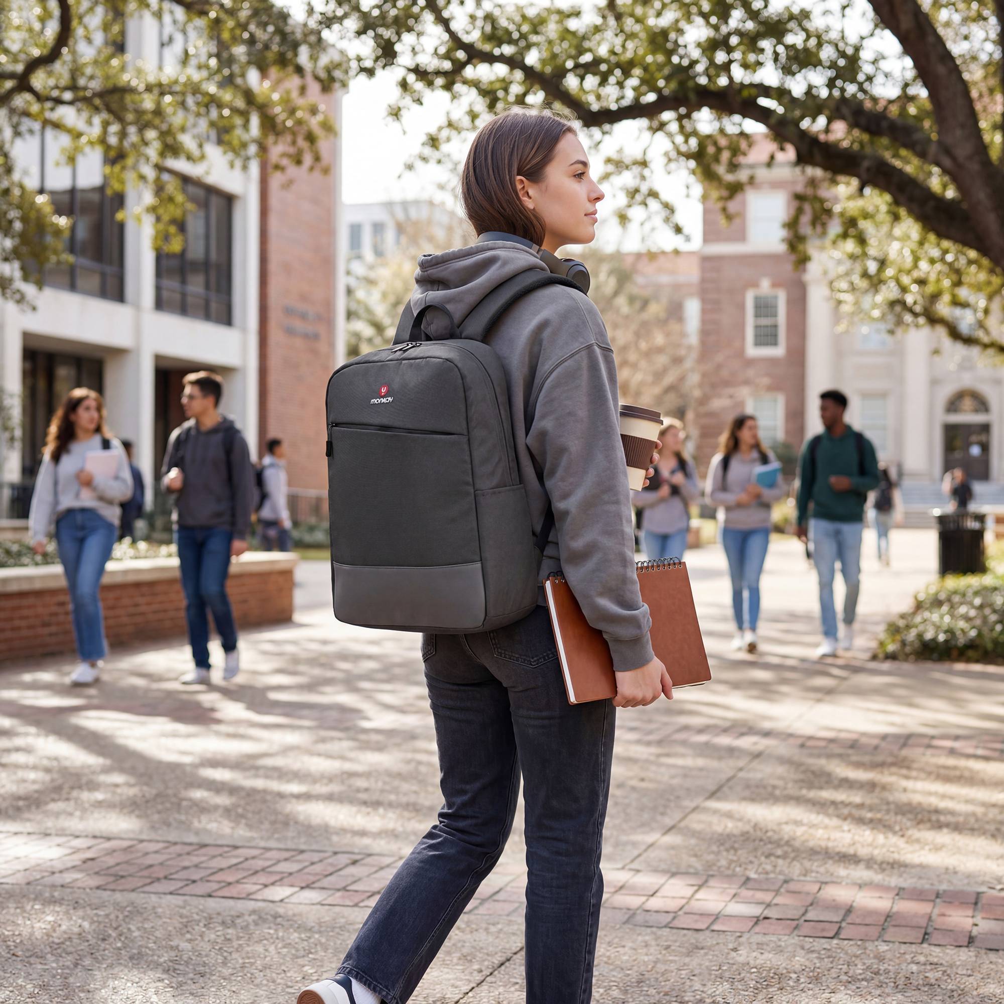 Una joven con mochila camina por un campus, sosteniendo una taza de café y un cuaderno.