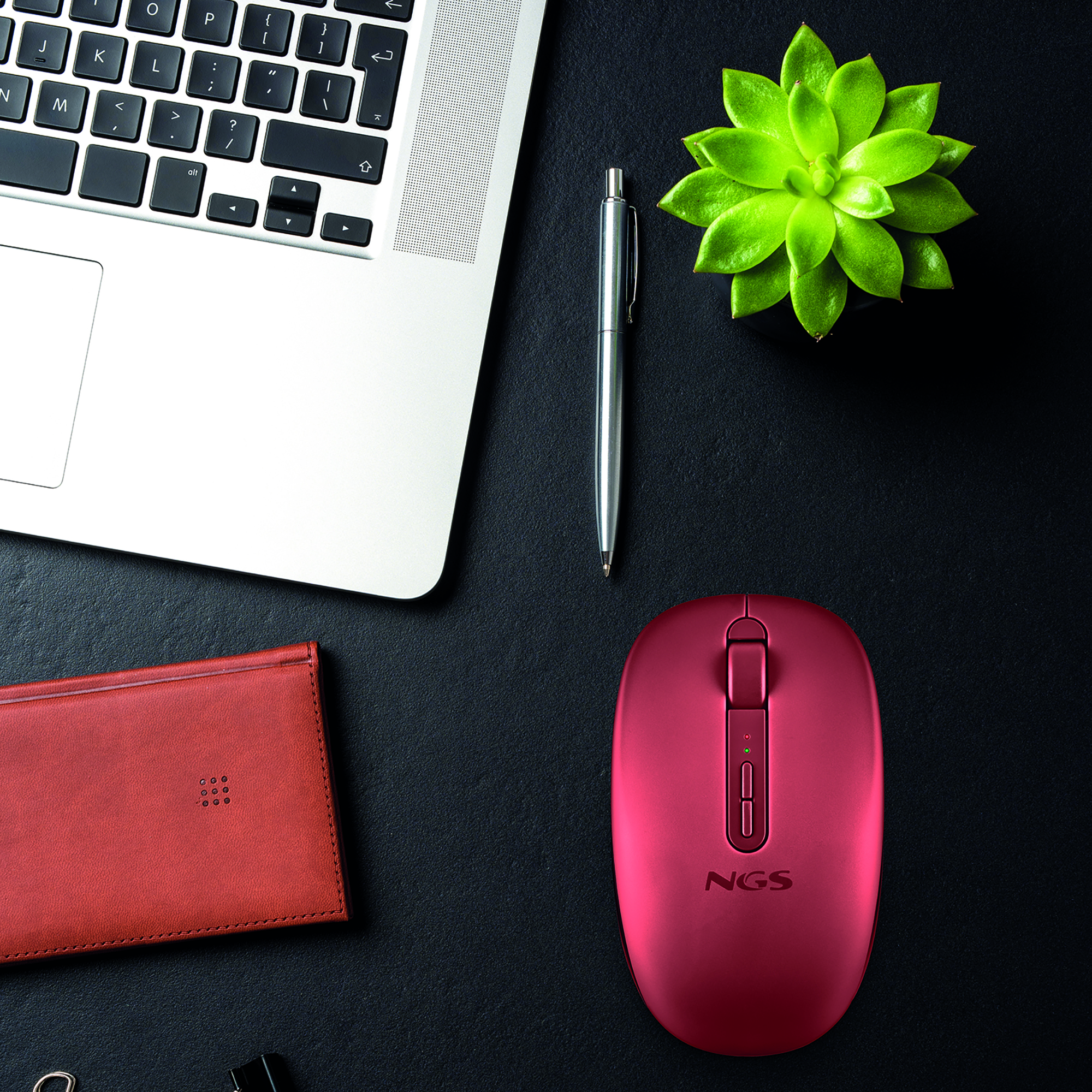 Un mouse NGS rosso, penna argentata, portafoglio marrone, laptop e pianta.