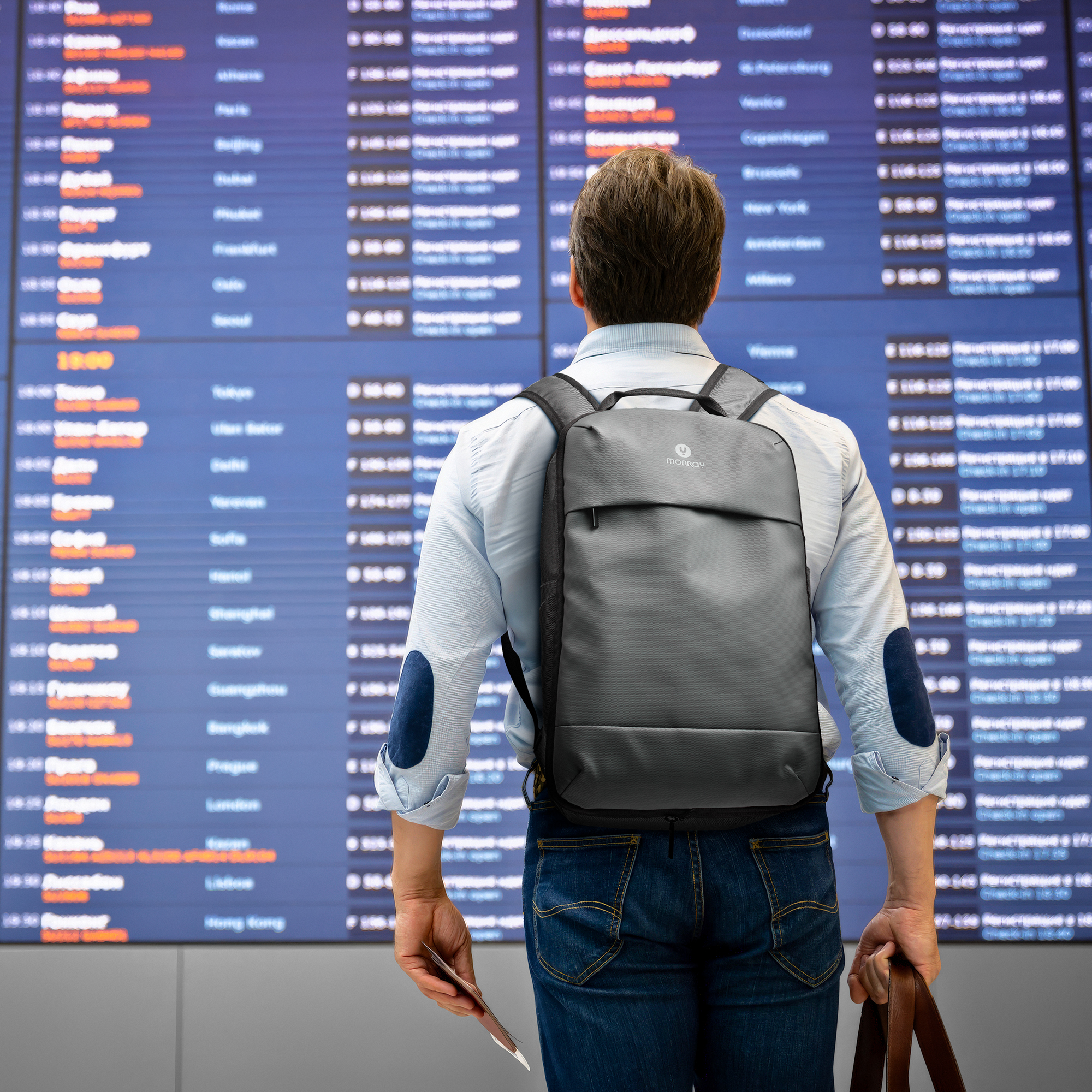 Hombre con mochila delante de tablero de información de vuelos con ciudades y horarios.