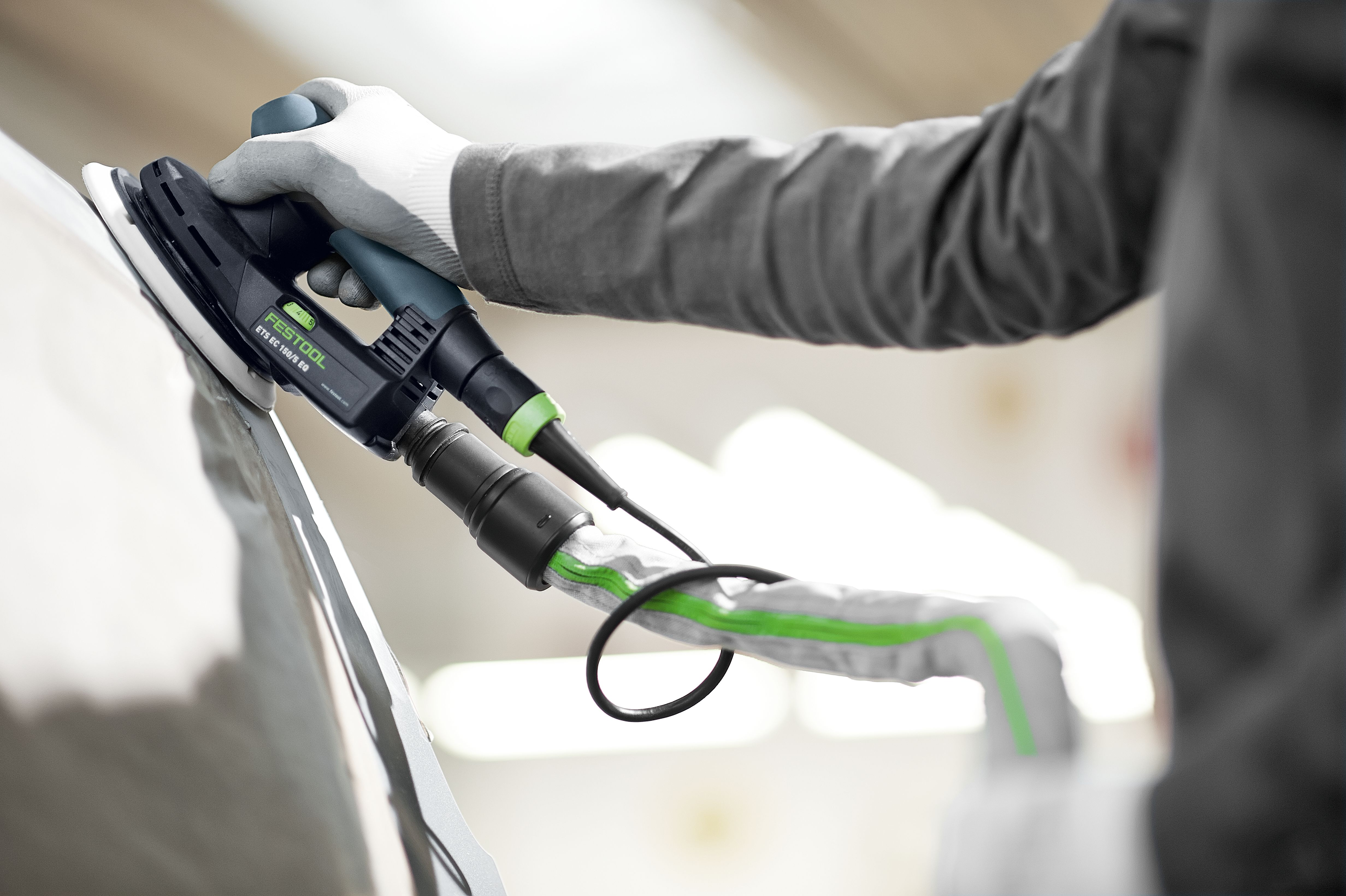 Mano guantata usa levigatrice Festool su superficie curva. Tubo collegato.