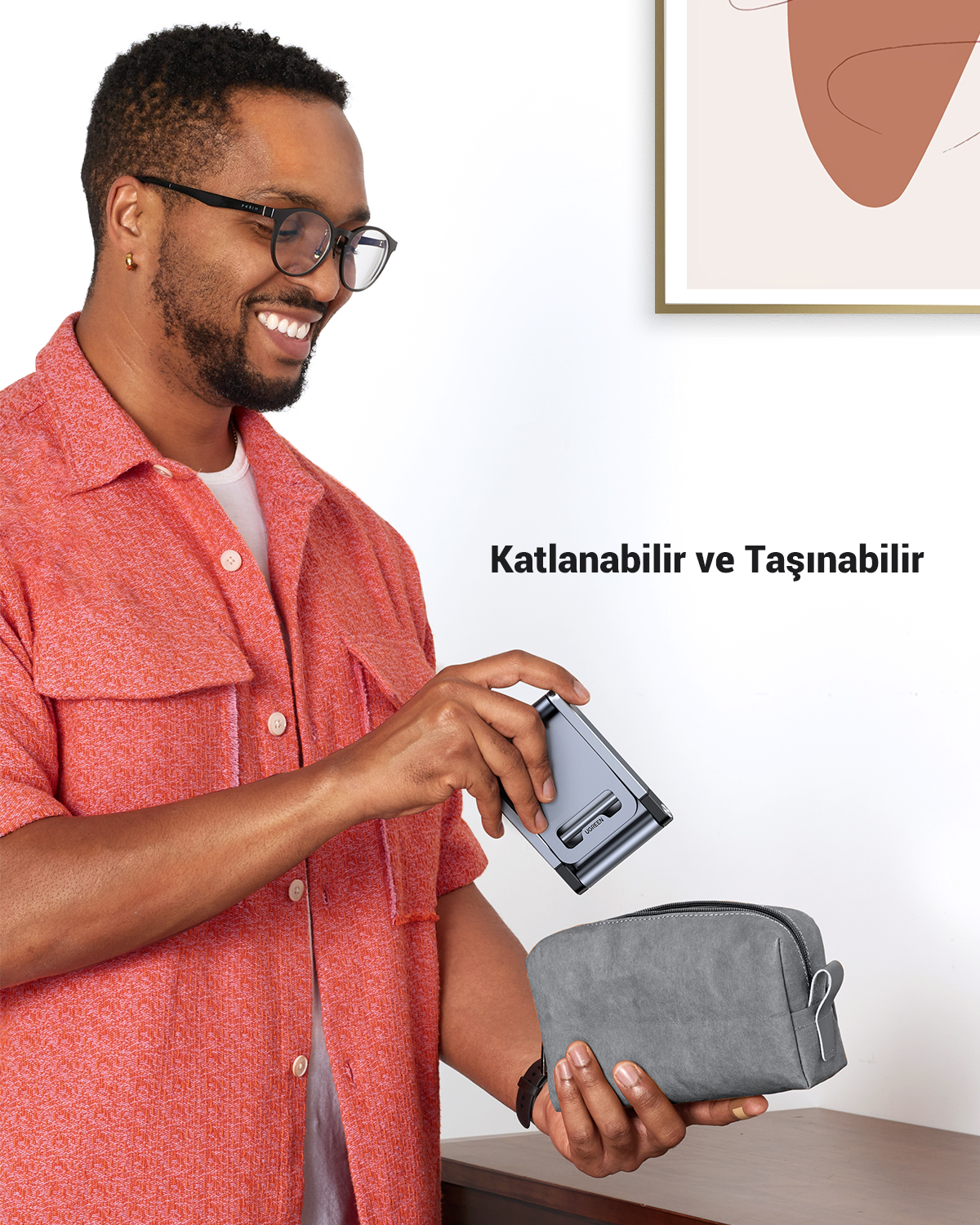 Ein Mann mit Brille und korallenrotem Hemd hält einen grauen Ständer über eine graue Tasche.