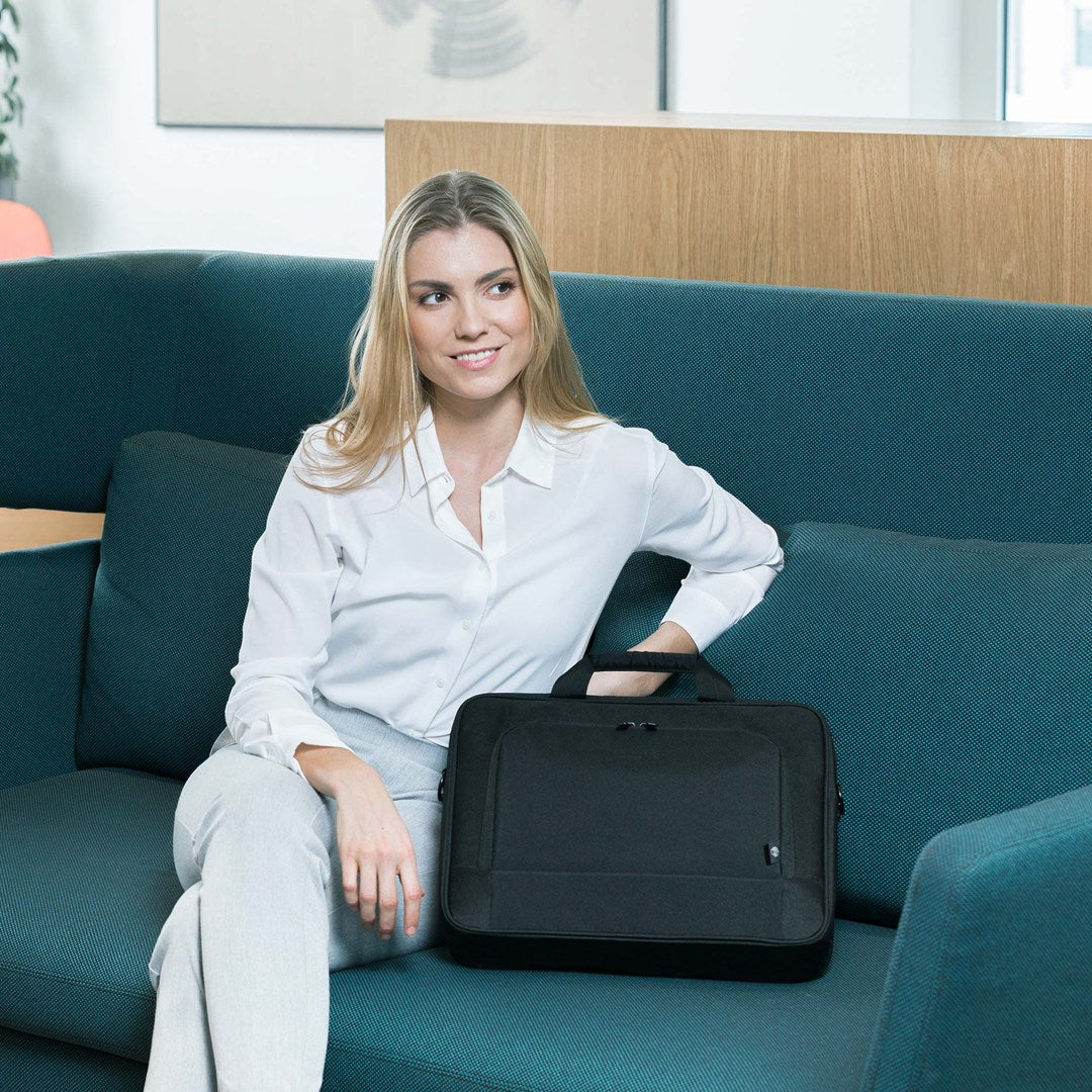 Una donna seduta su un divano turchese con una borsa per laptop nera accanto.