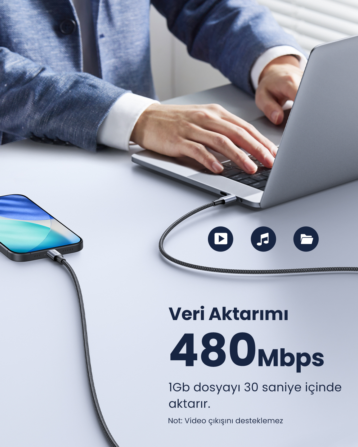 Ein Mann tippt auf einem Laptop, während ein Kabel von einem Handy zu ihm führt.