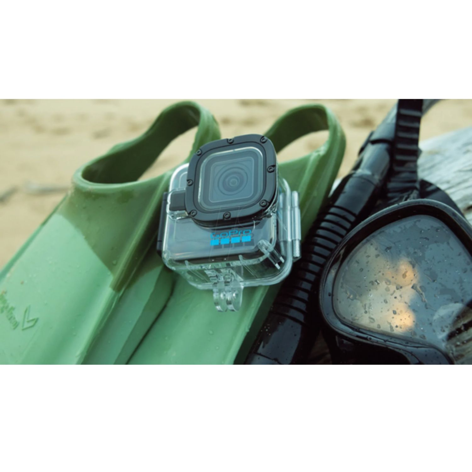 Grüne Flossen, GoPro und eine Schnorcheltaucherbrille mit Wassertropfen auf Sand.