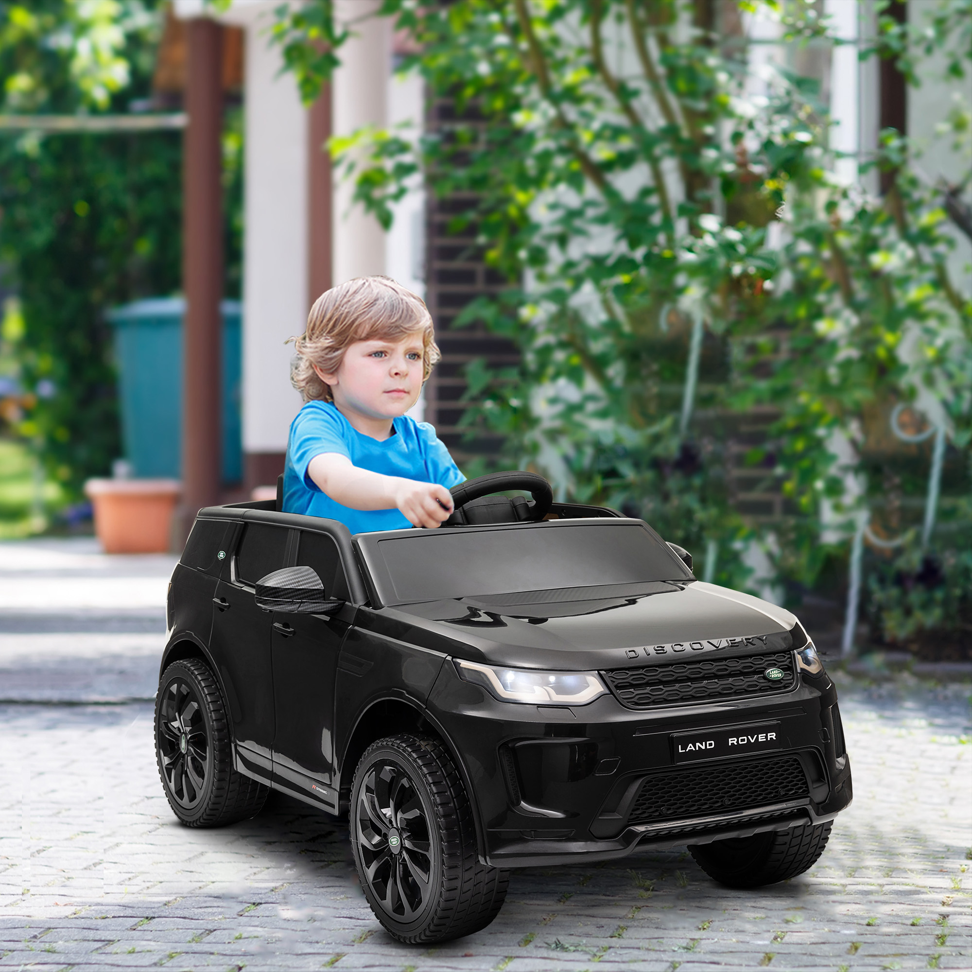 Un bambino guida una macchina giocattolo nera su un vialetto pavimentato.