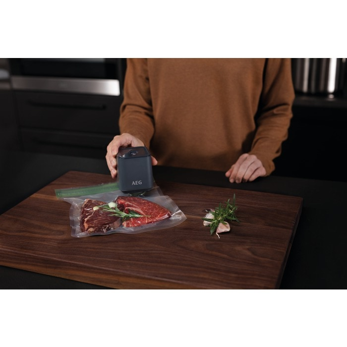 Un sellador al vacío AEG sella carne en una bolsa sobre una tabla de madera.
