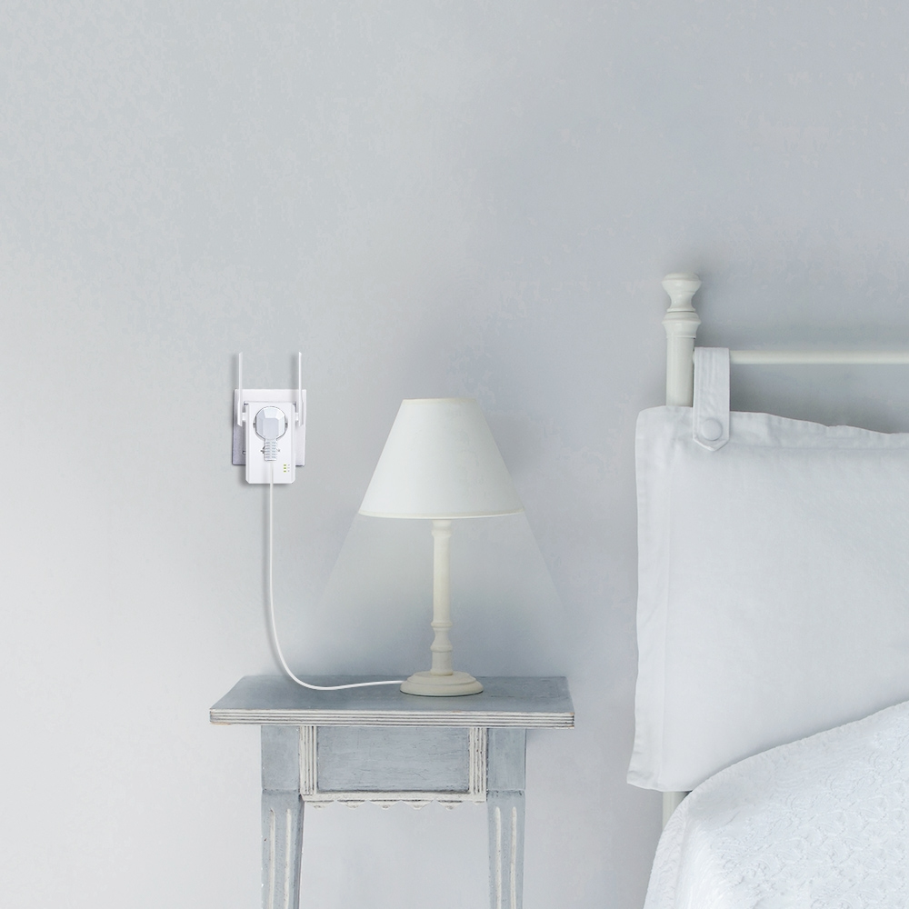 A WiFi extender and a lamp sit on a nightstand next to a bed.