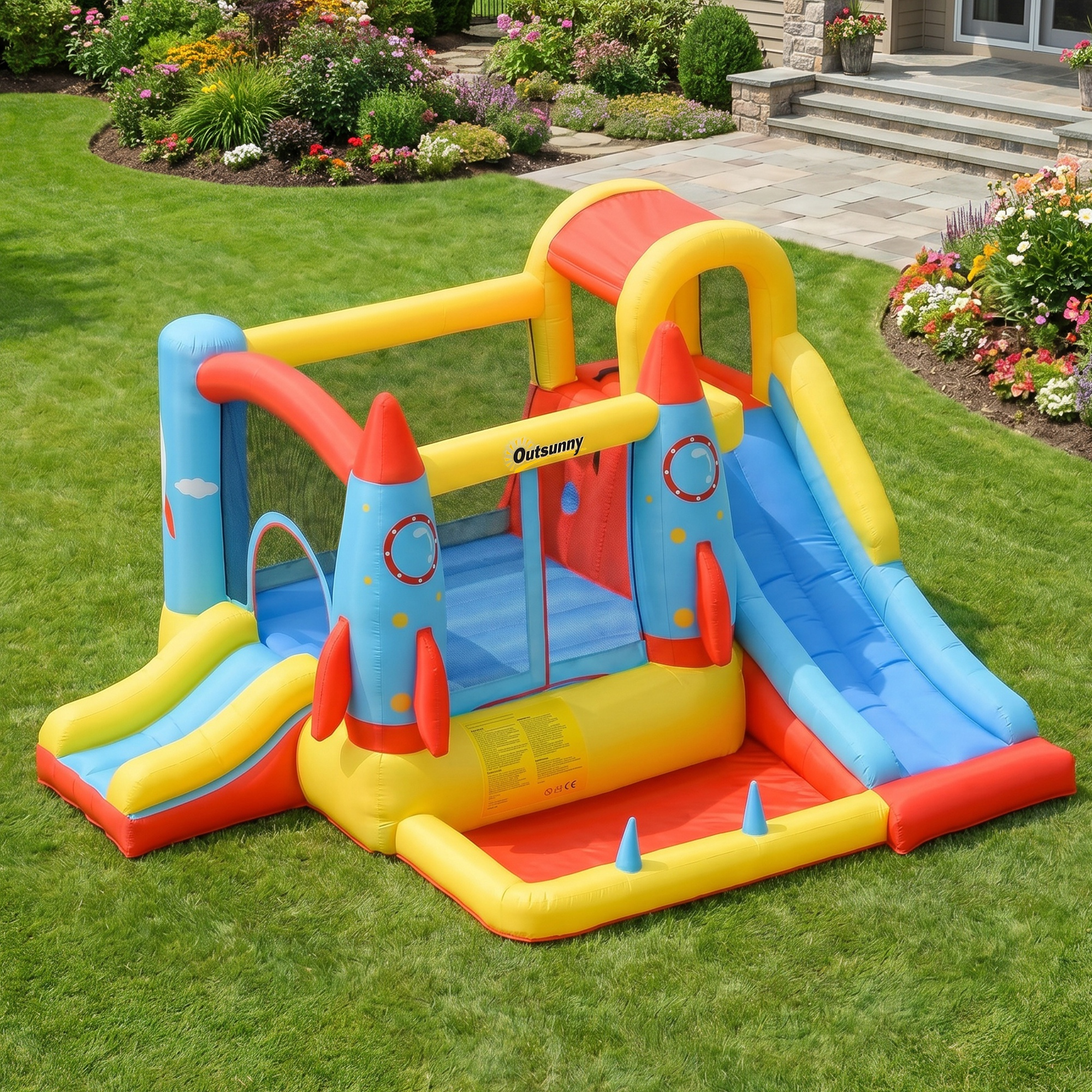 Casa inflable de cohete con toboganes en césped verde, frente a parterres.