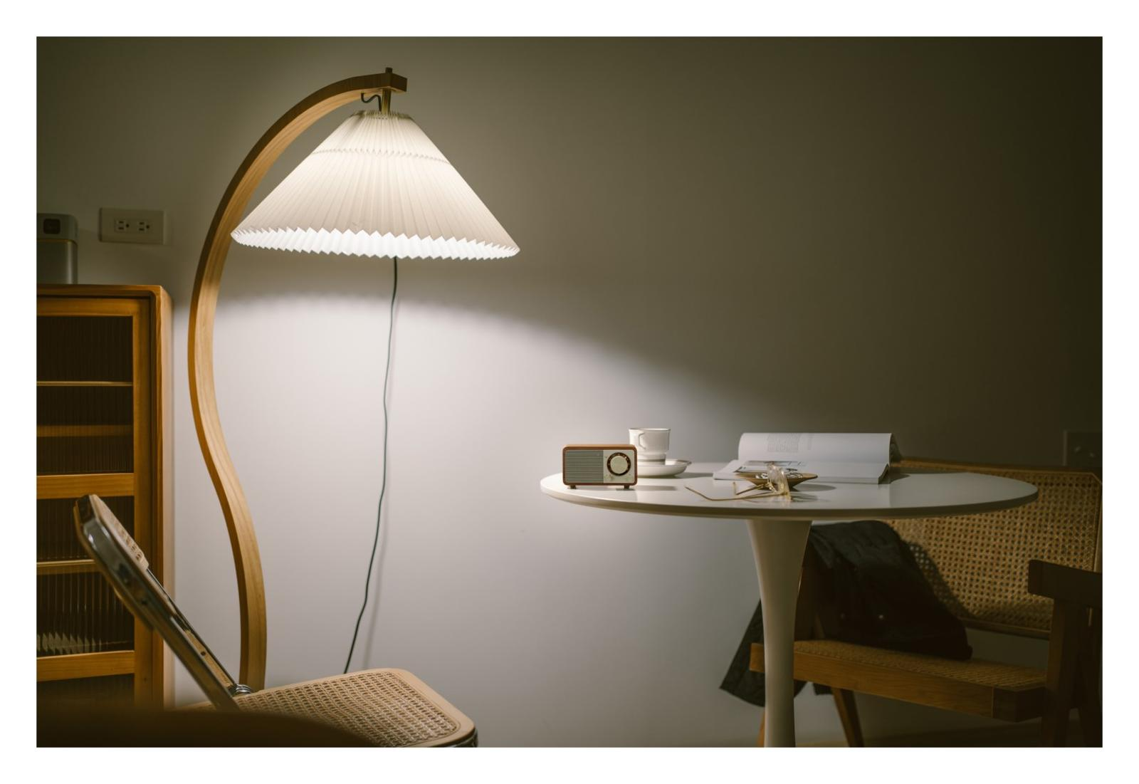 Ein Bogenlampenschirm beleuchtet einen runden Tisch mit einem Radio, Tasse und Buch.
